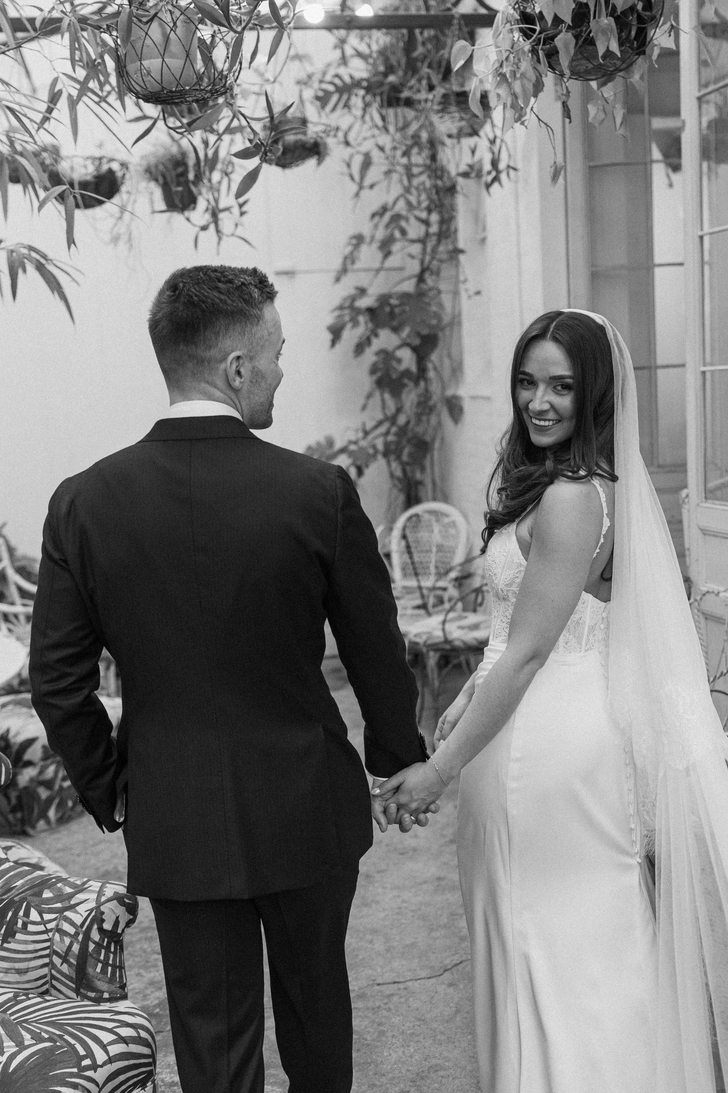 Black and white photo of smiling bride in white gown and veil holding hands with groom in black suit.