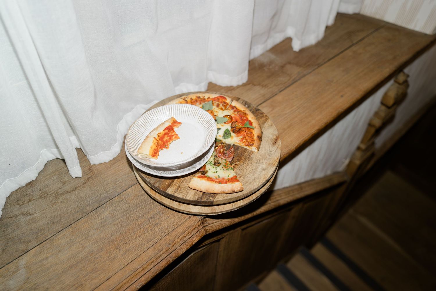 Rustic wooden shelf with pizza slices on a wooden board and white plates at a wedding reception.