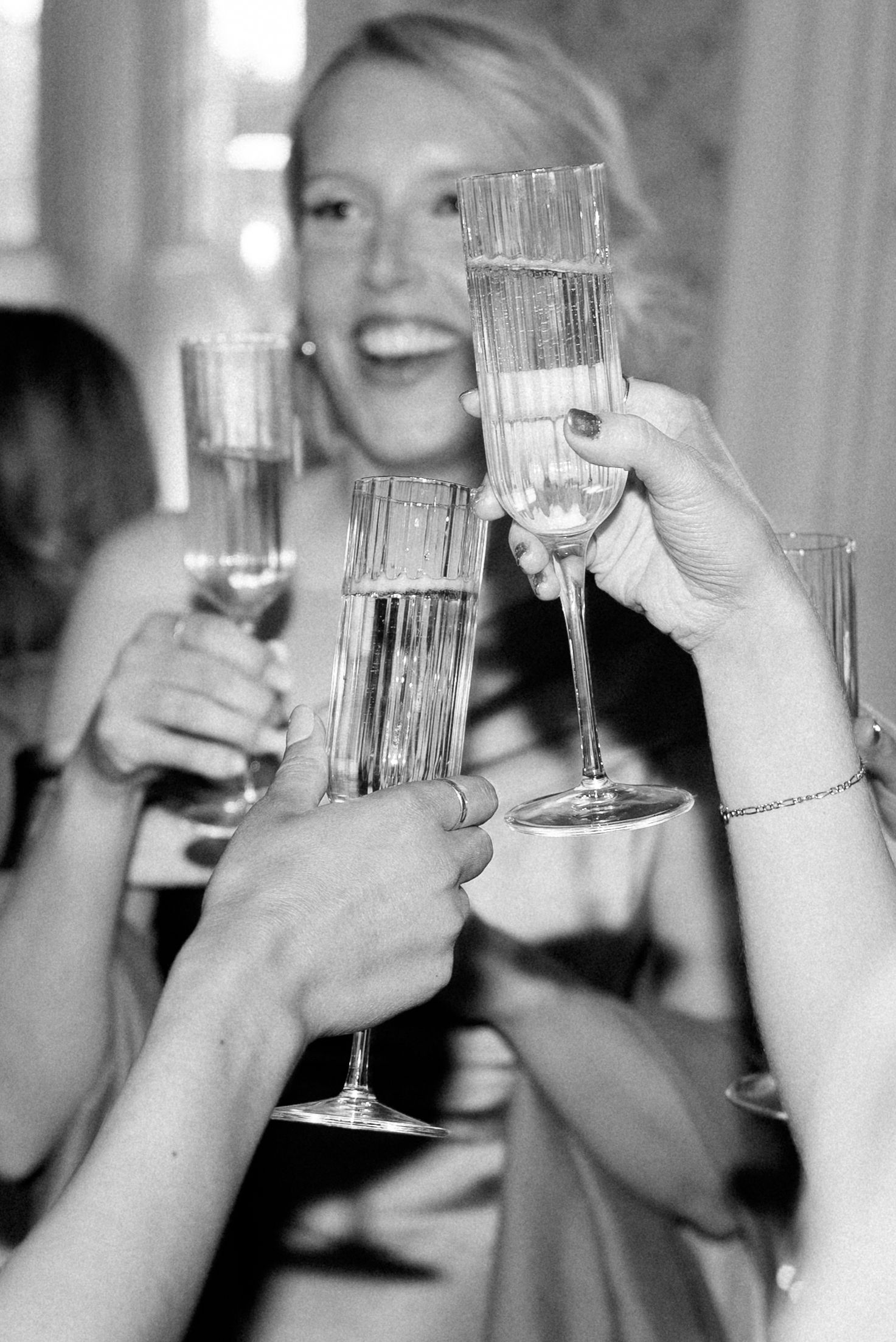 Smiling blonde wedding guest raises champagne flute in celebratory toast with others at reception.