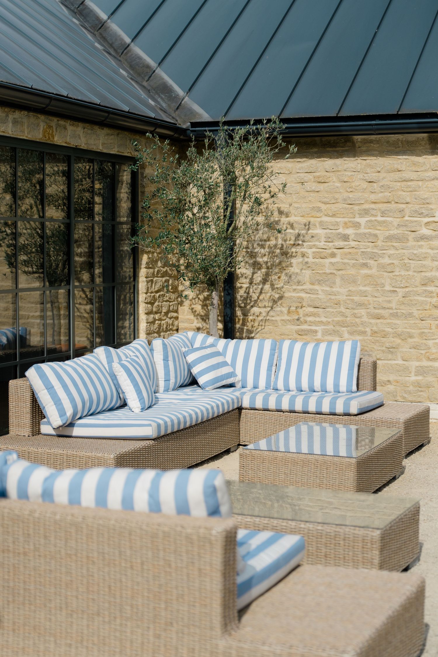 Elegant outdoor seating area with blue and white striped cushions beside a Cotswolds stone building.