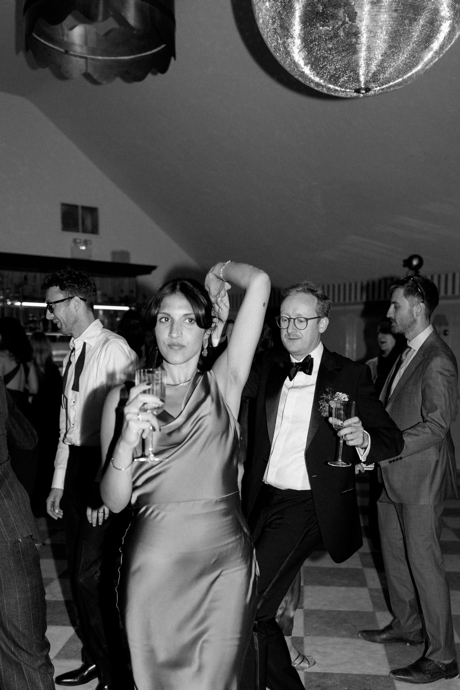 Black and white photo of guests dancing under disco ball at elegant evening wedding reception party.