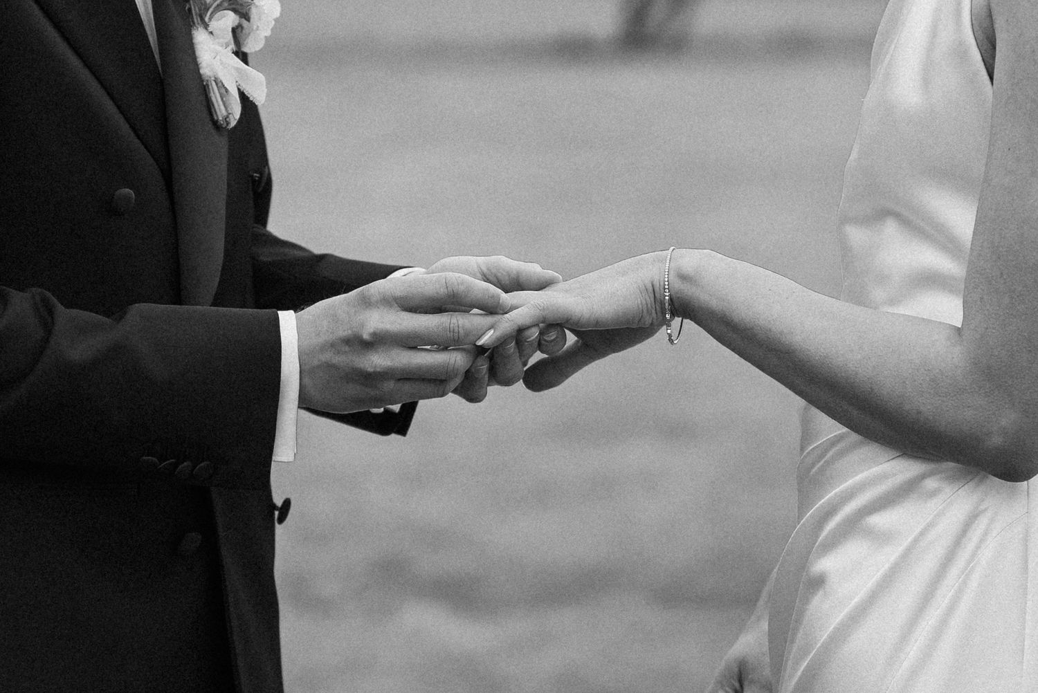 Close-up black and white photo of groom placing wedding ring on brides finger during ceremony.