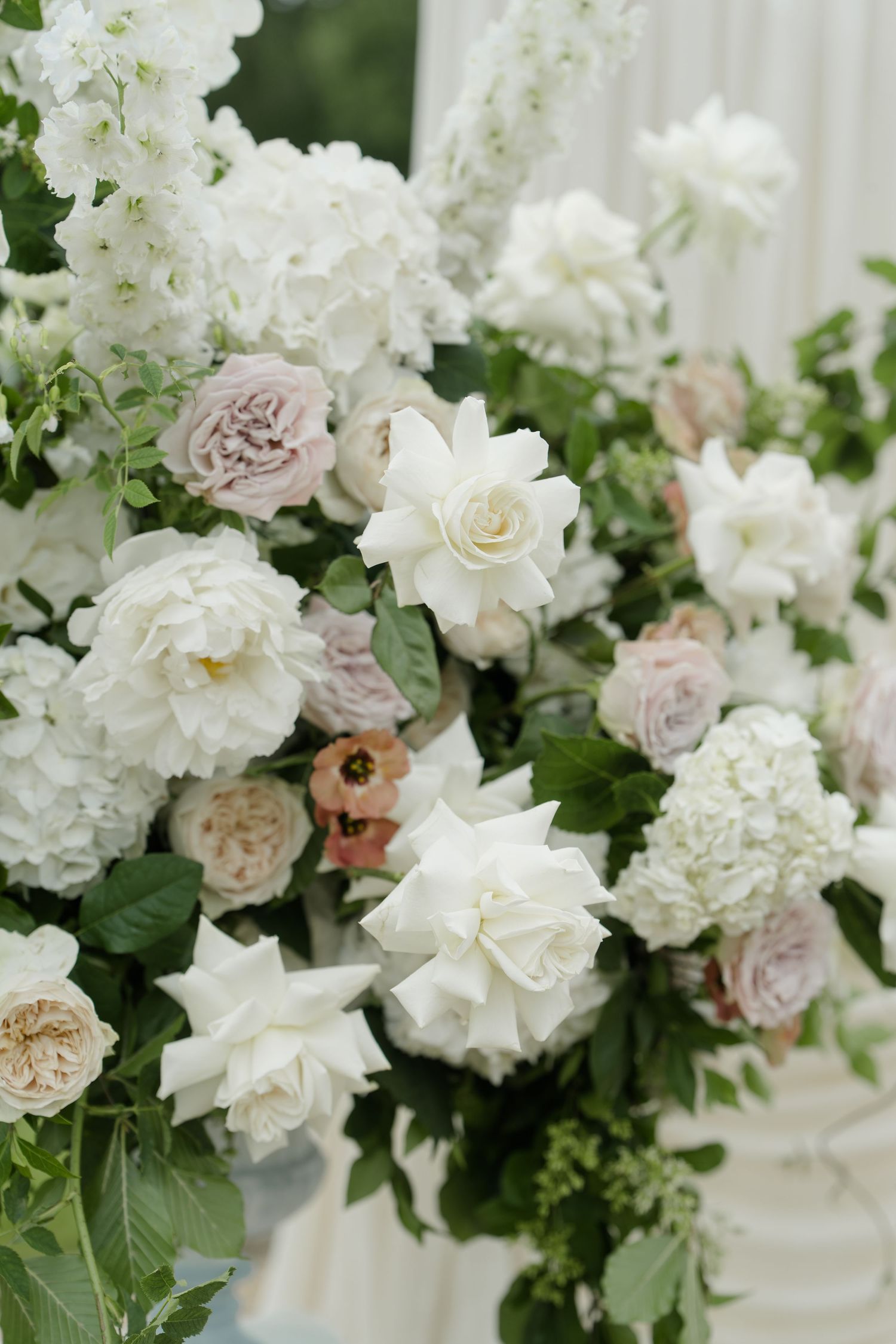 Lush wedding floral arrangement featuring white peonies, roses, hydrangeas, and blush blooms with greenery.
