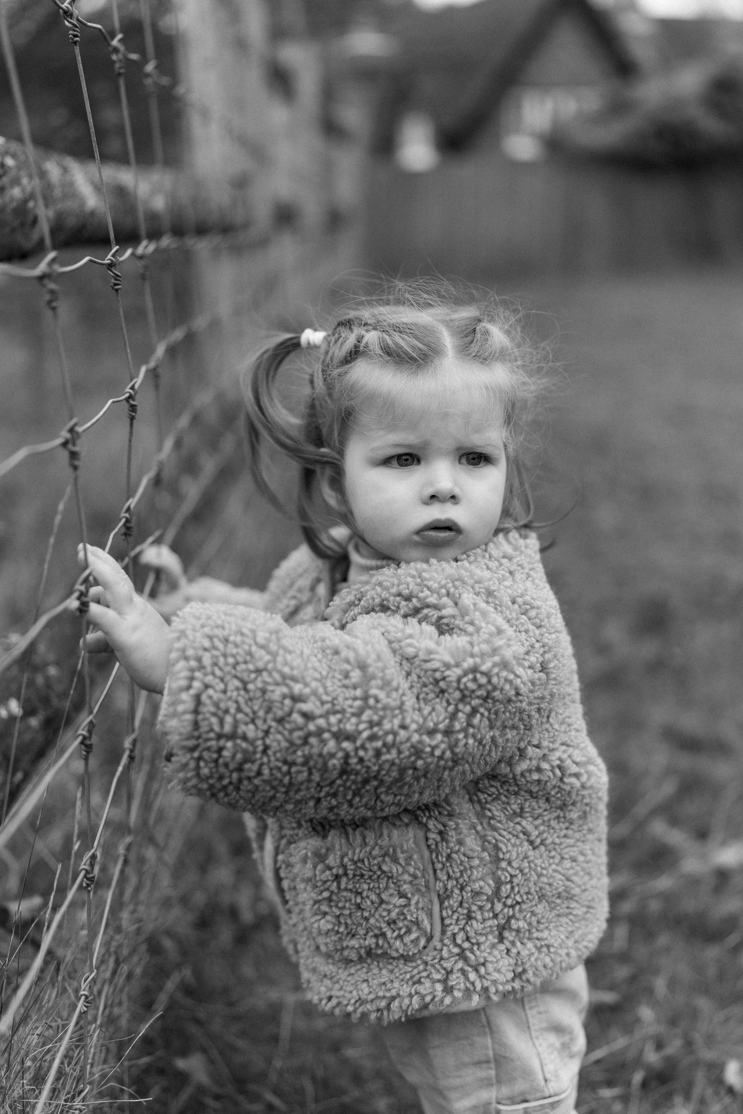 Black and white image of a toddler in a fuzzy coat playing outdoors.