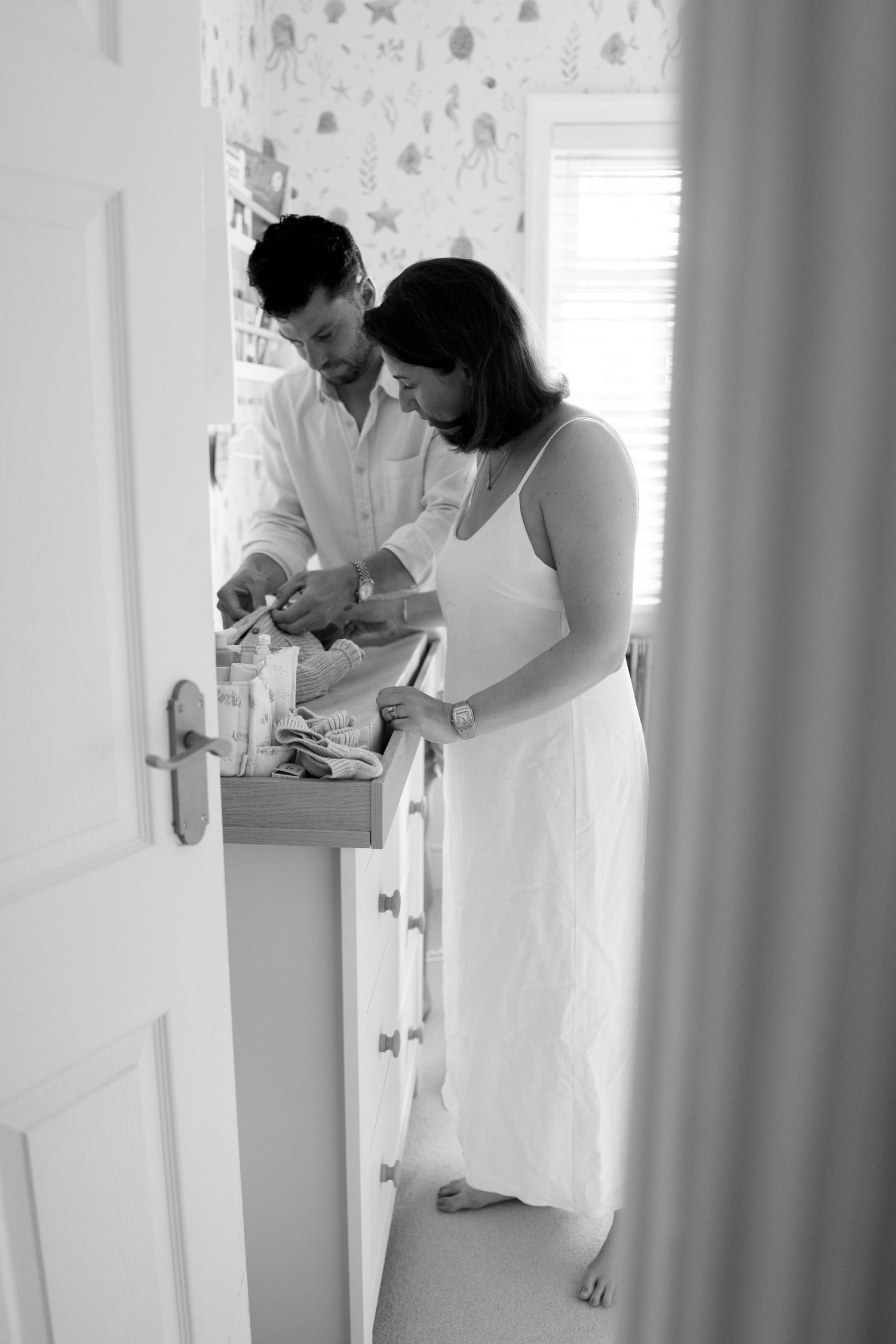 Couple in white clothing standing together in bright interior hallway.