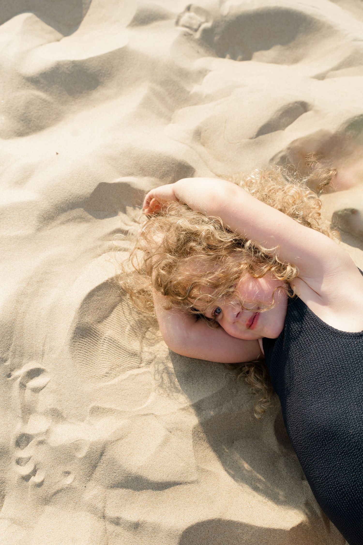 Person in black swimsuit lying on textured beach sand.