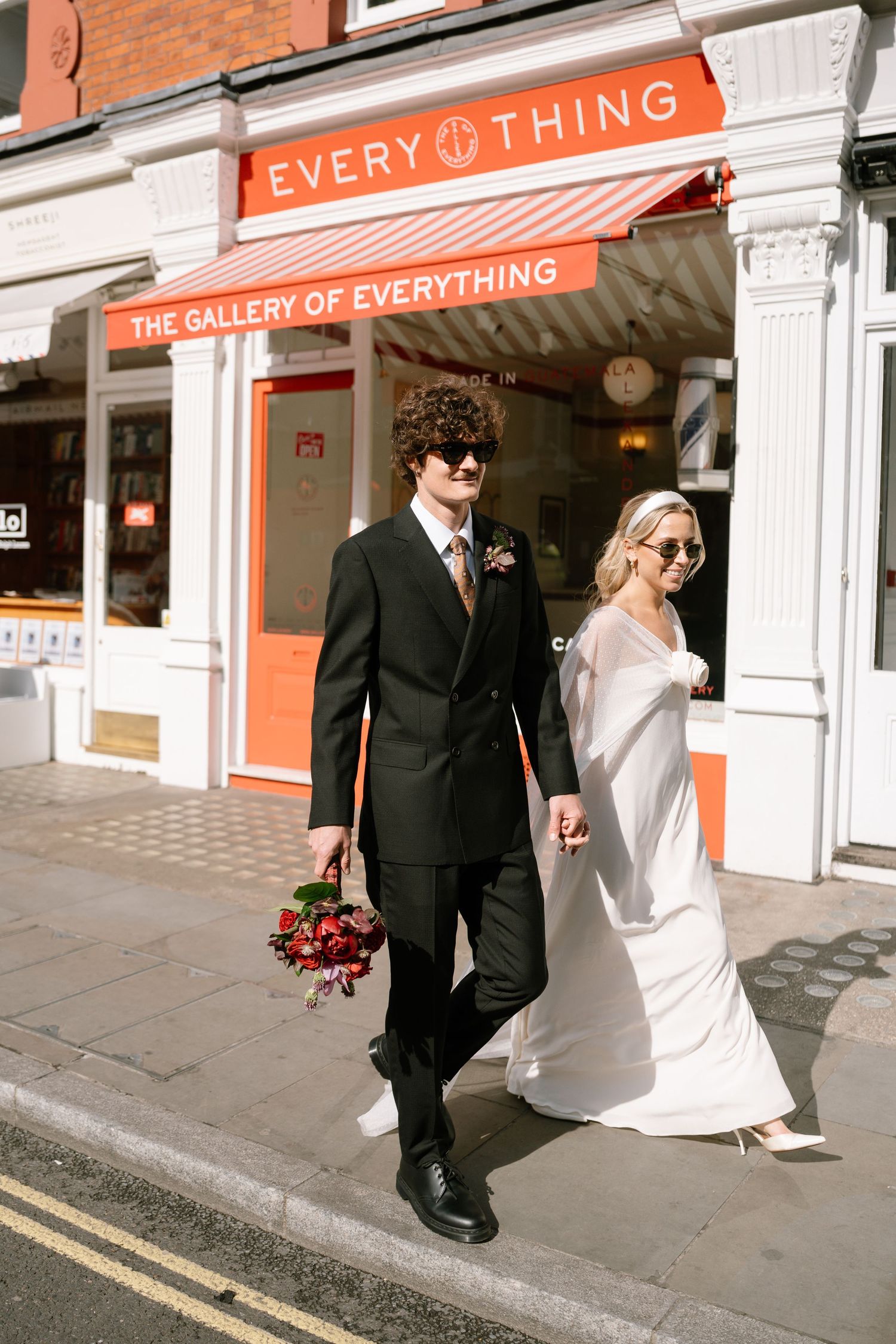 Newlyweds walking past The Gallery of Everything storefront with orange signage.