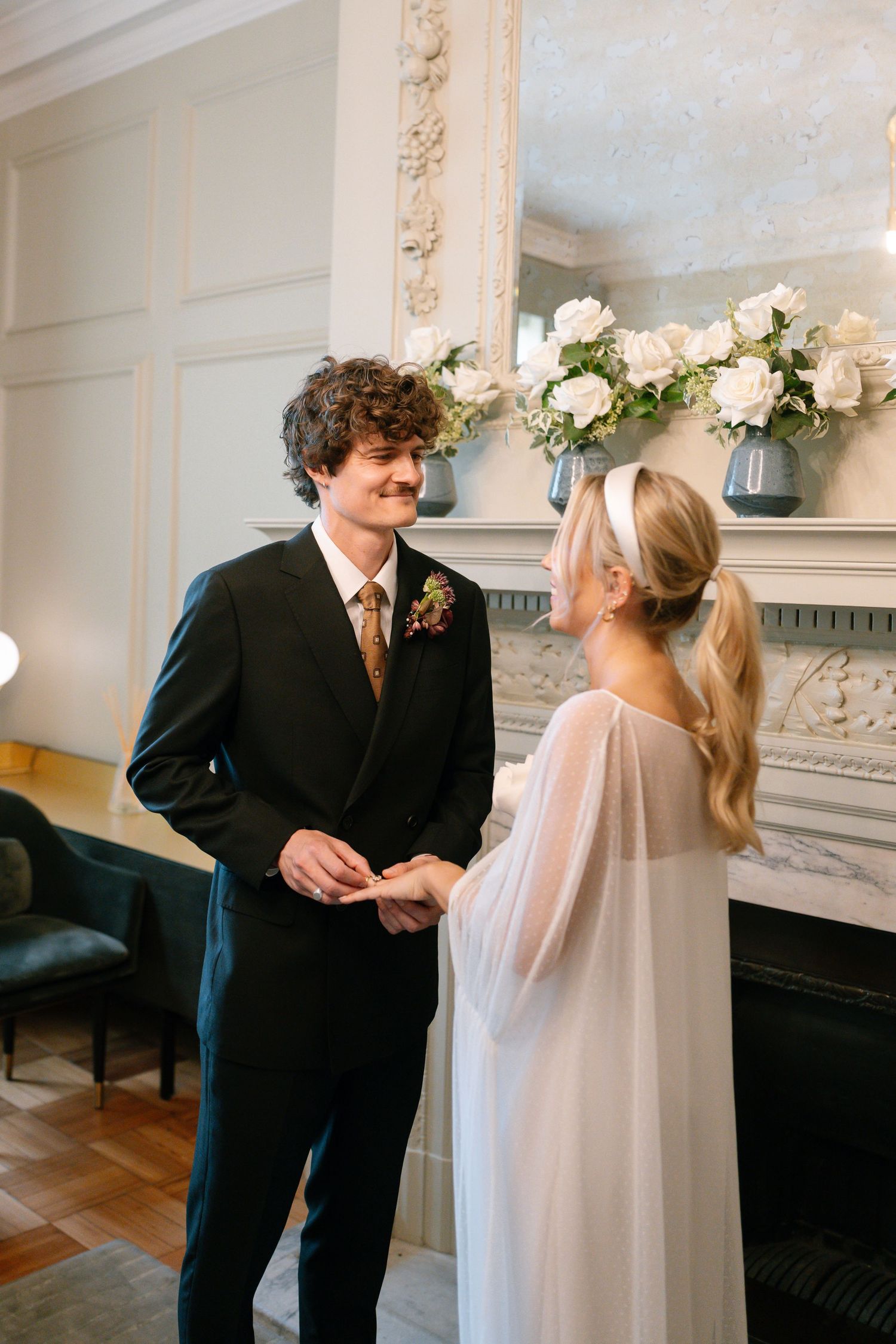 Couple exchanging rings in front of a decorated fireplace during intimate ceremony.