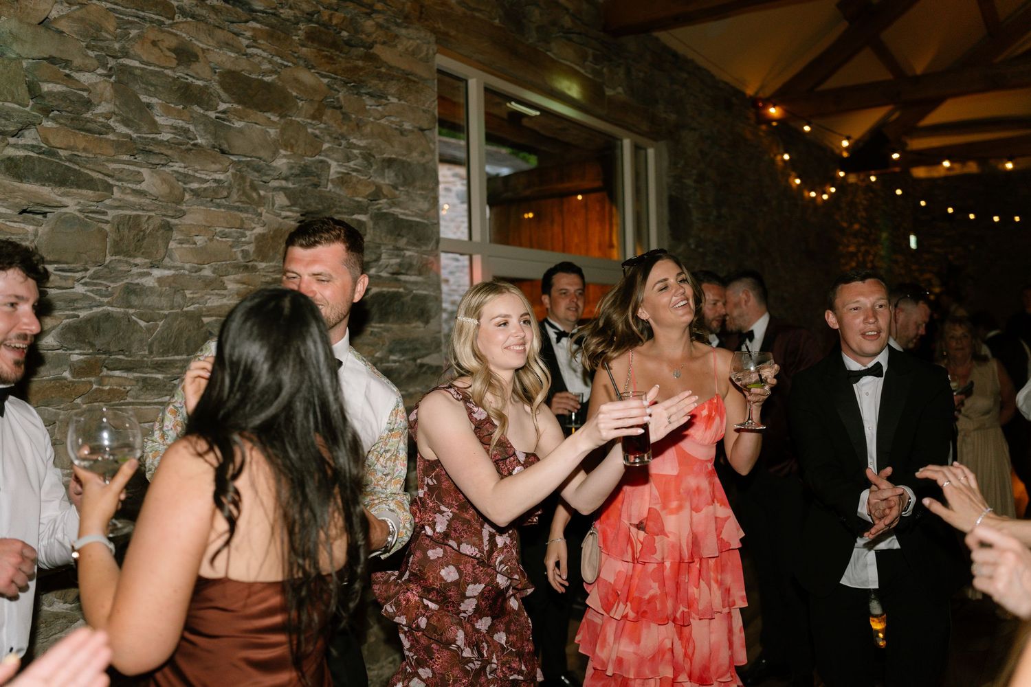 Partygoers dancing and mingling in a dimly lit stone-walled venue with string lights overhead.