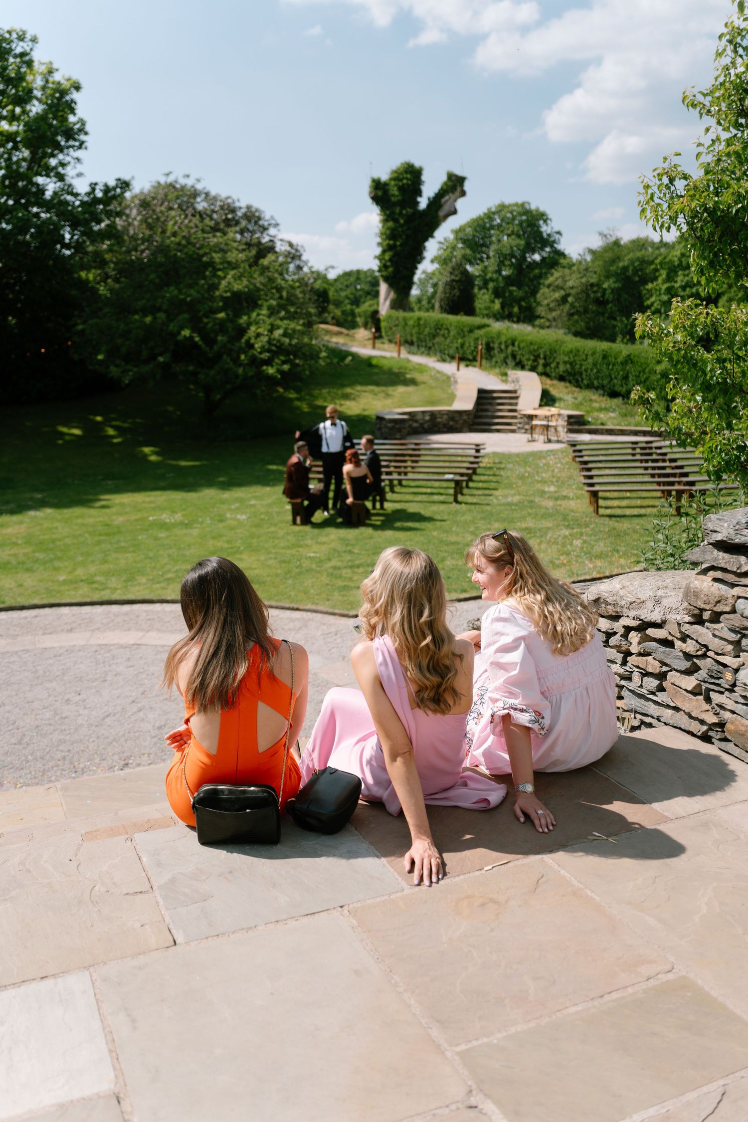Three people sit together on stone steps overlooking a sunny green landscape.