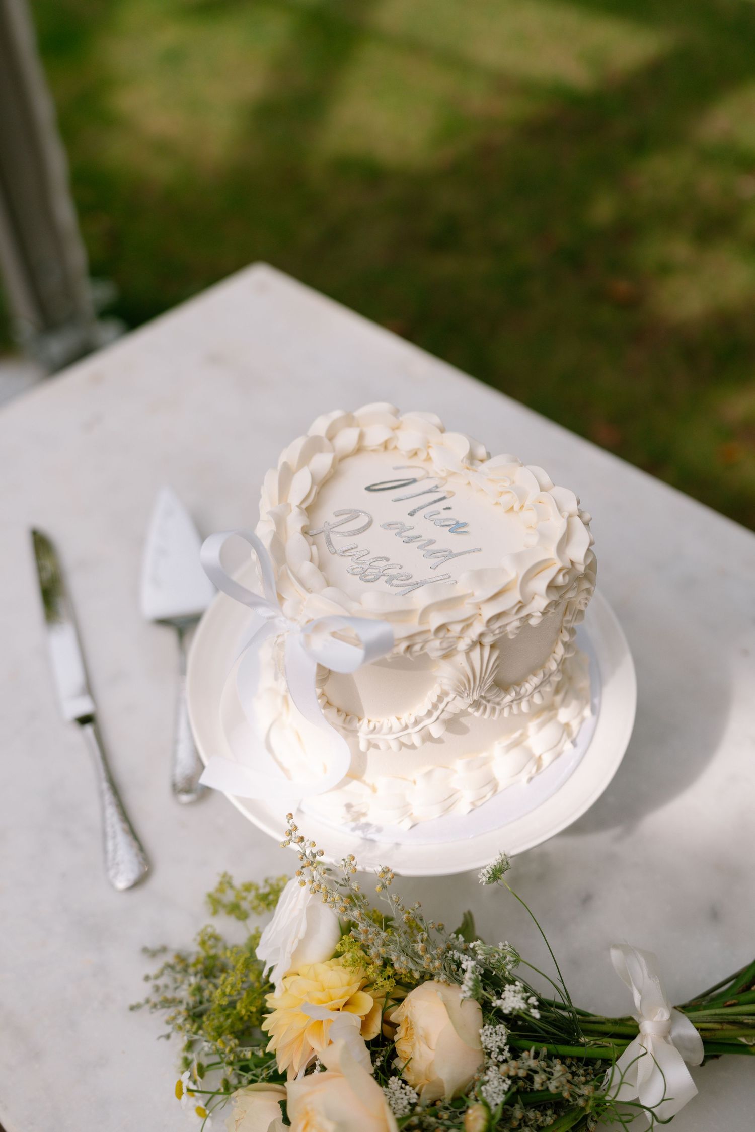 Wedding cake decorated with white frosting and fresh flowers on outdoor table.