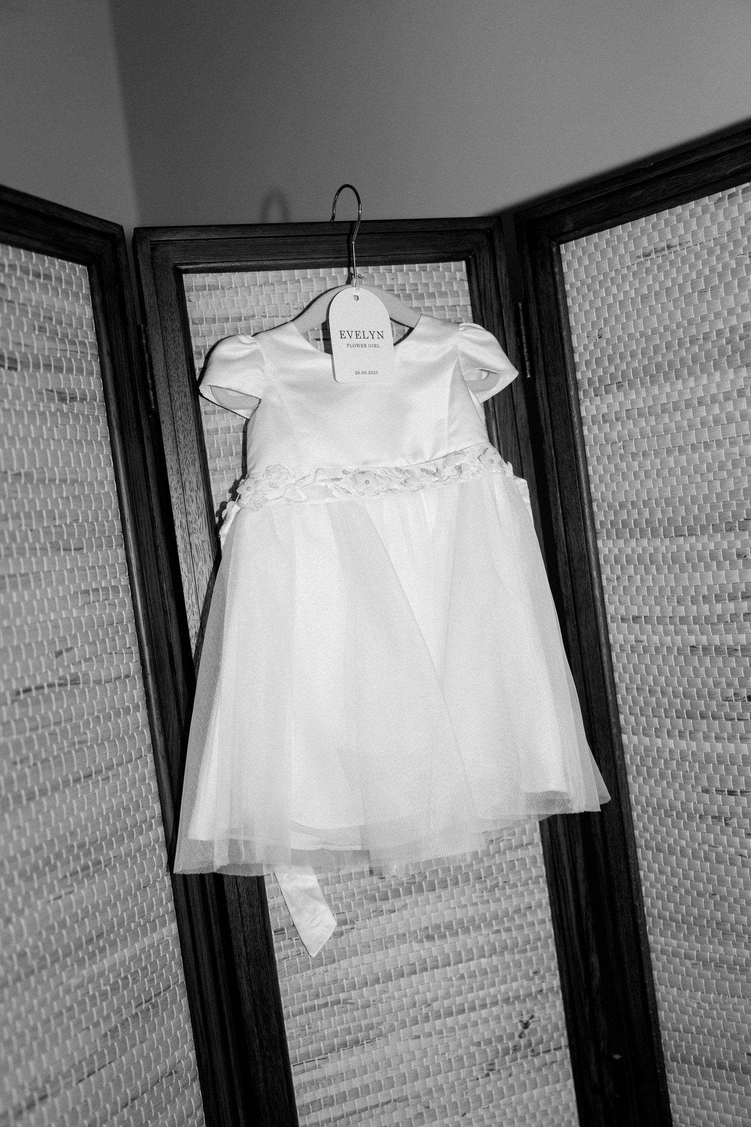 White baby dresses hanging in a row on dark wooden hangers.