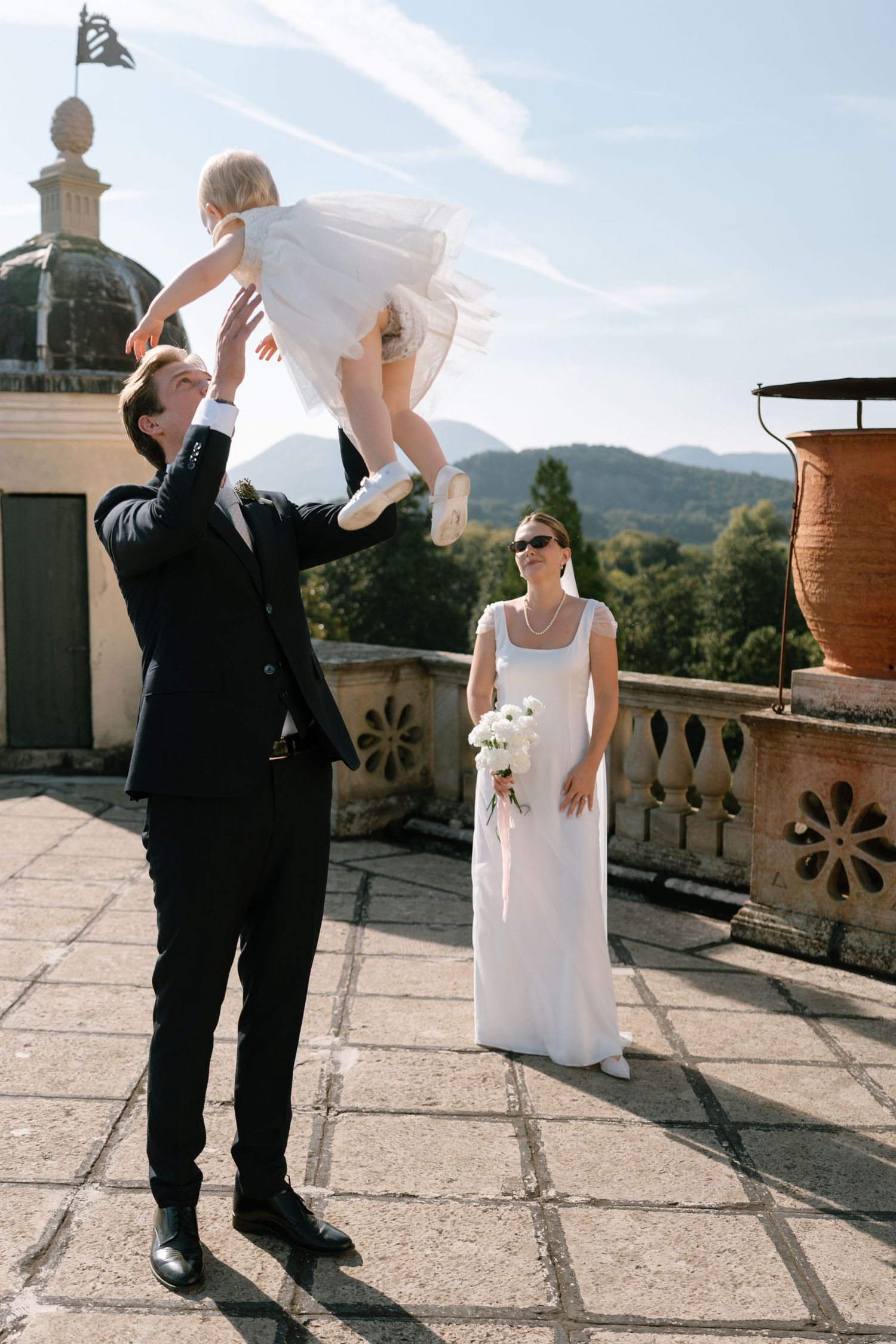 Joyful wedding moment captured on castle terrace with mountain backdrop.