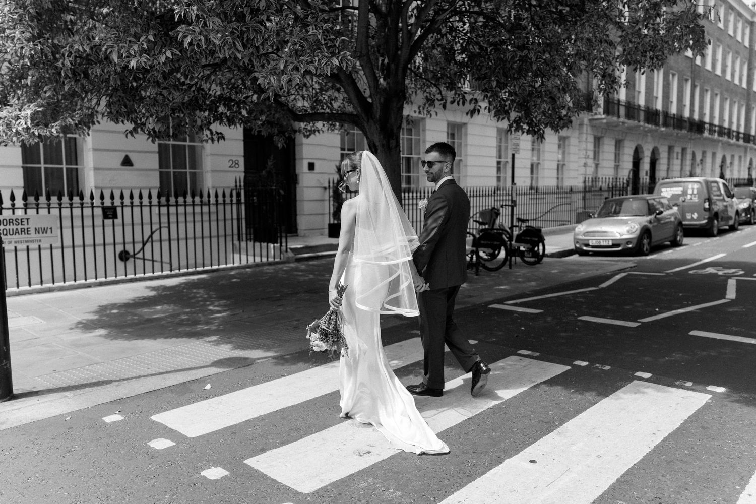 Bride and groom cross a zebra crossing on a London street in a classic black and white wedding photo.
