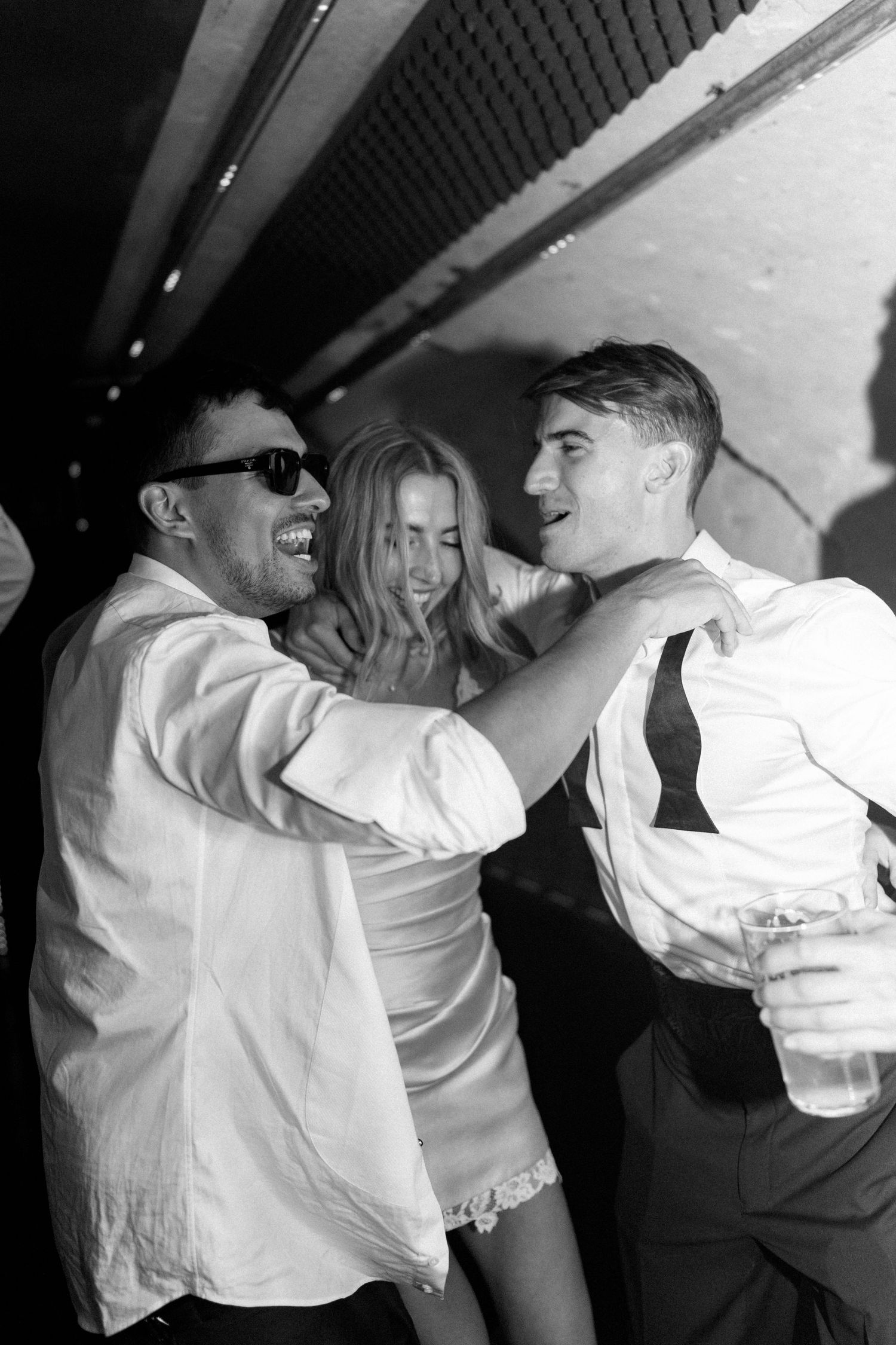 Black and white photo of guests laughing and dancing together at a lively wedding reception.
