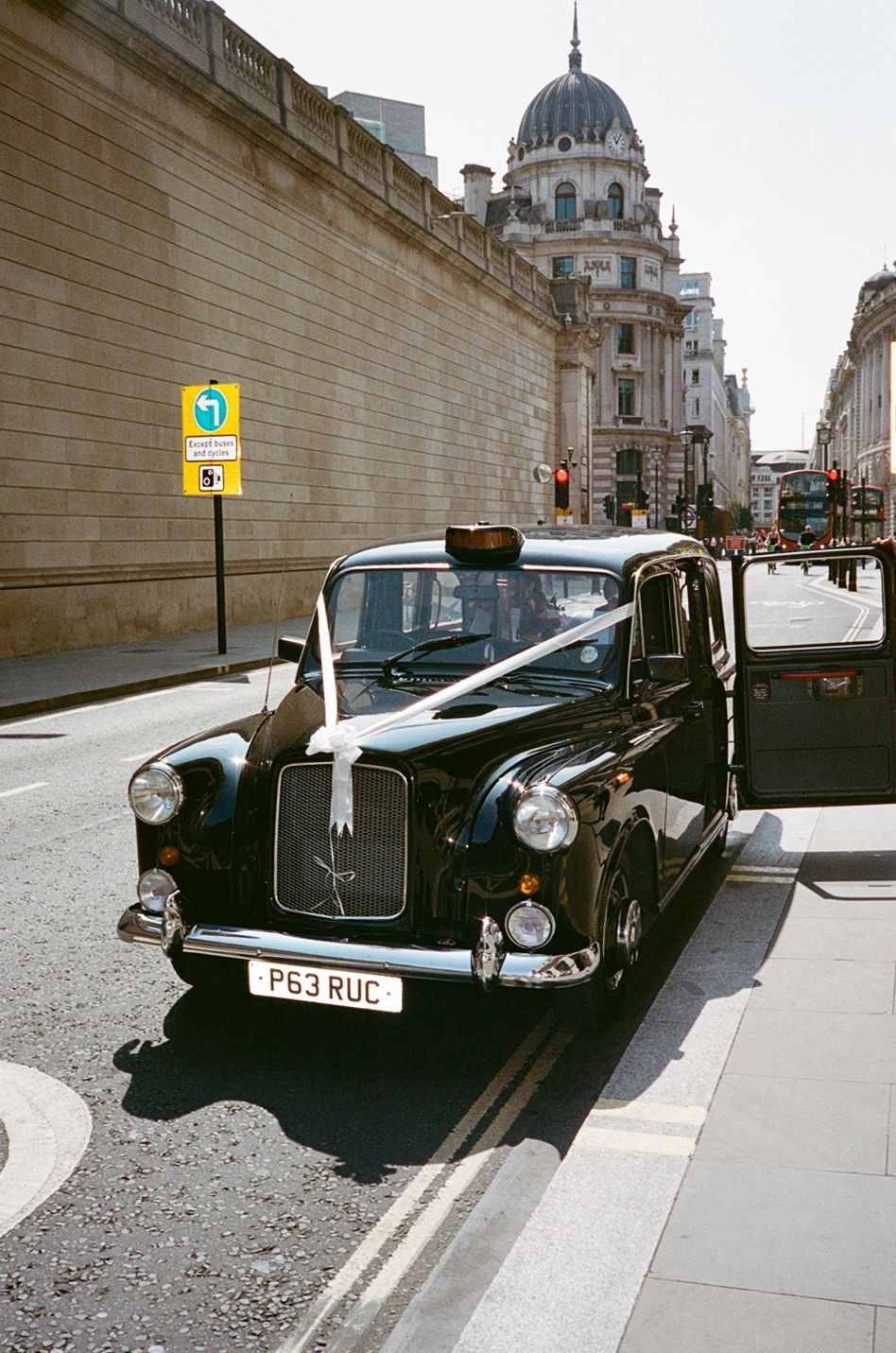 Classic black London taxi cab with white ribbon decoration parked on a city street near a grand domed building.