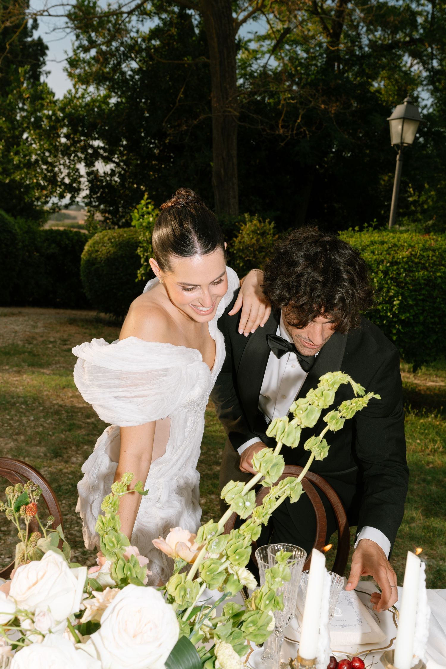 A couple arranges flowers and table settings at an elegant outdoor wedding reception.
