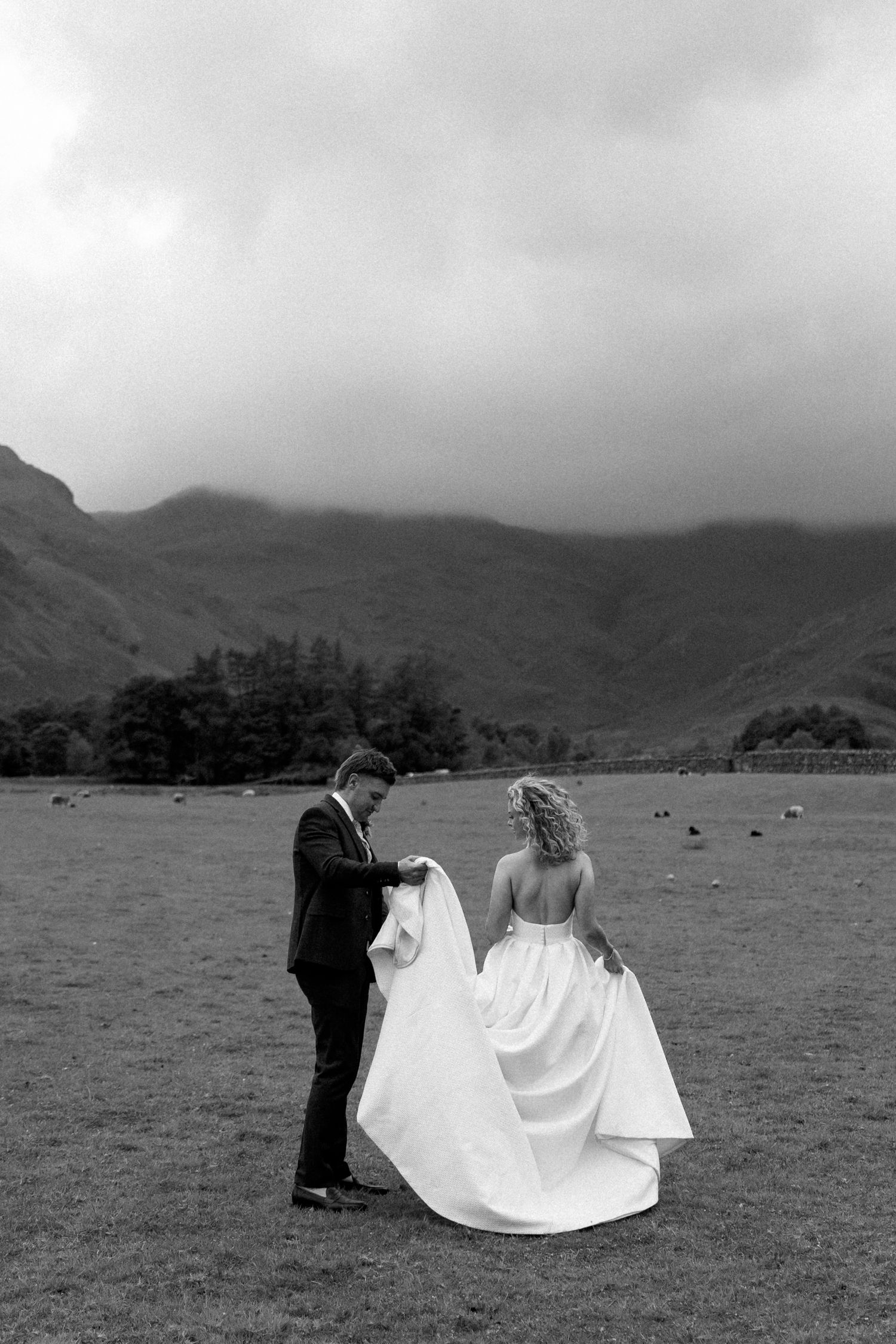 Dramatic black and white photo of a bride's dress flowing in the wind against mountain landscape.