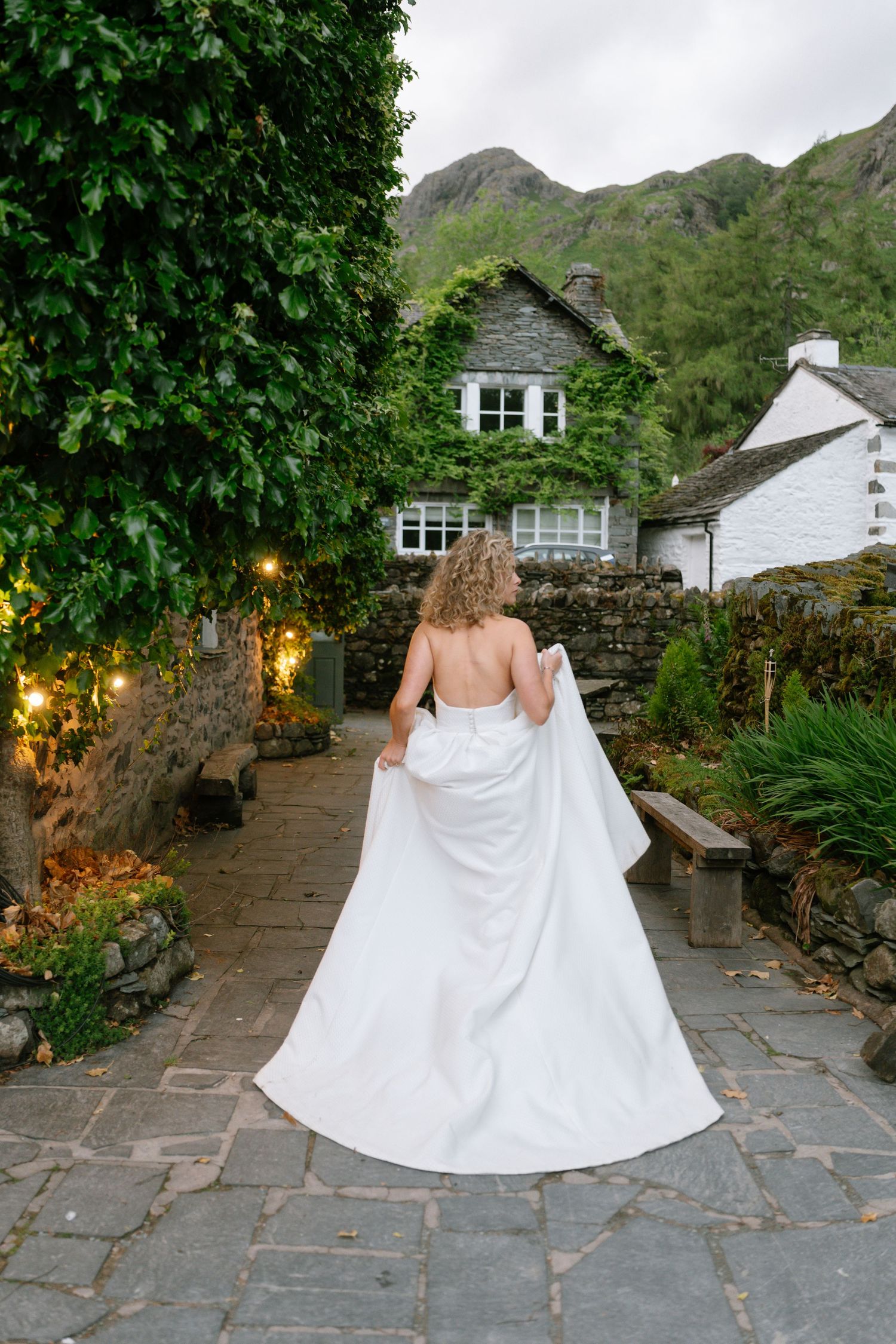 A bride walks along a stone pathway with mountain views and garden lighting.