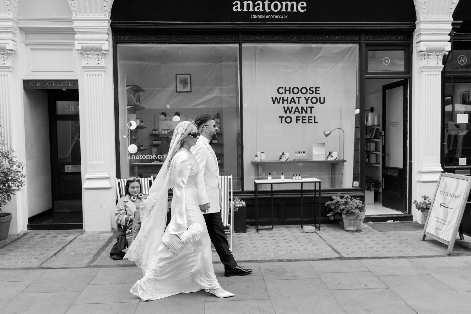 Black and white photo of people walking past an Anatome storefront with signage in the window.