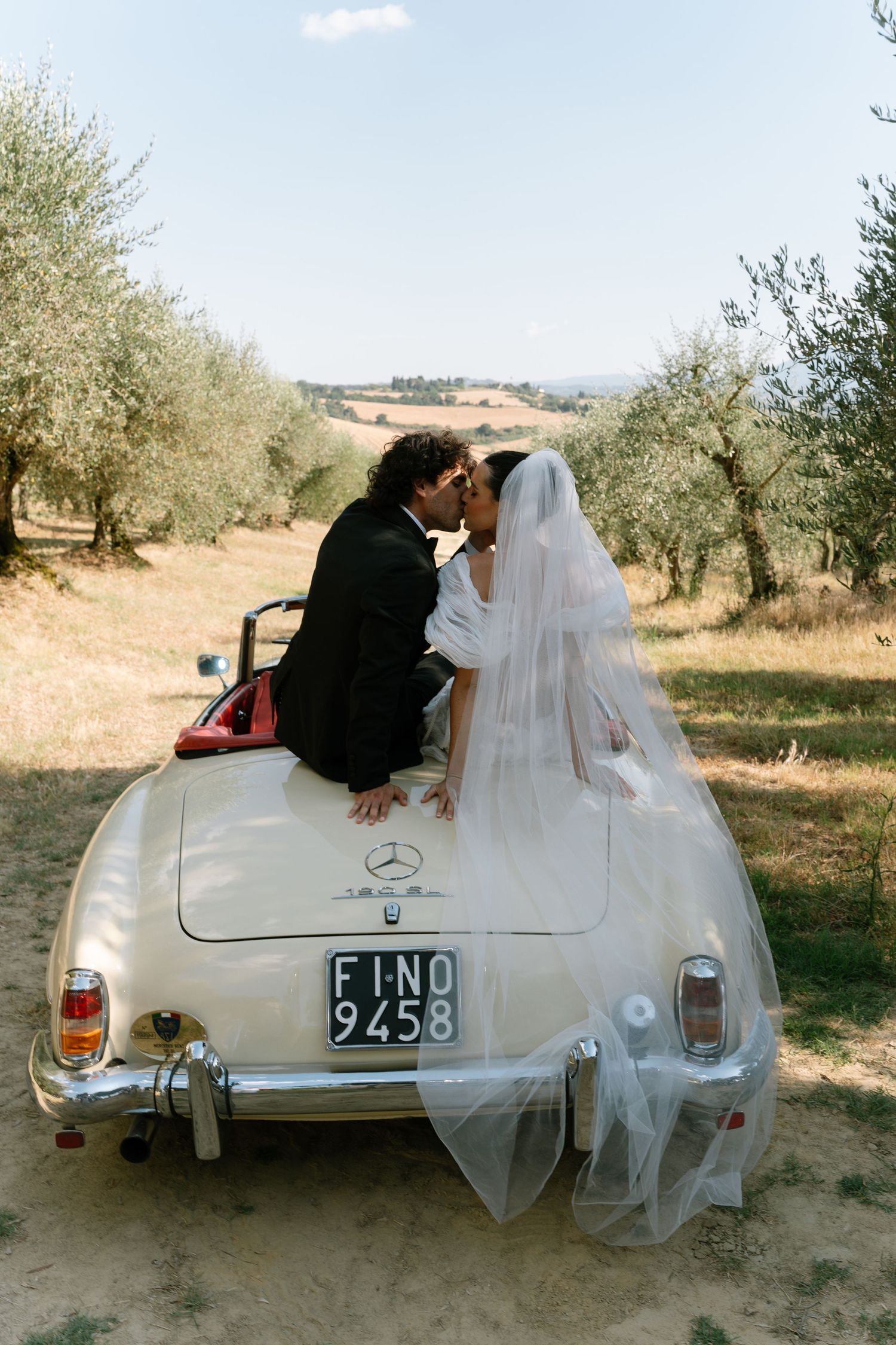 Classic white Mercedes-Benz convertible parked in an olive grove on a sunny day.