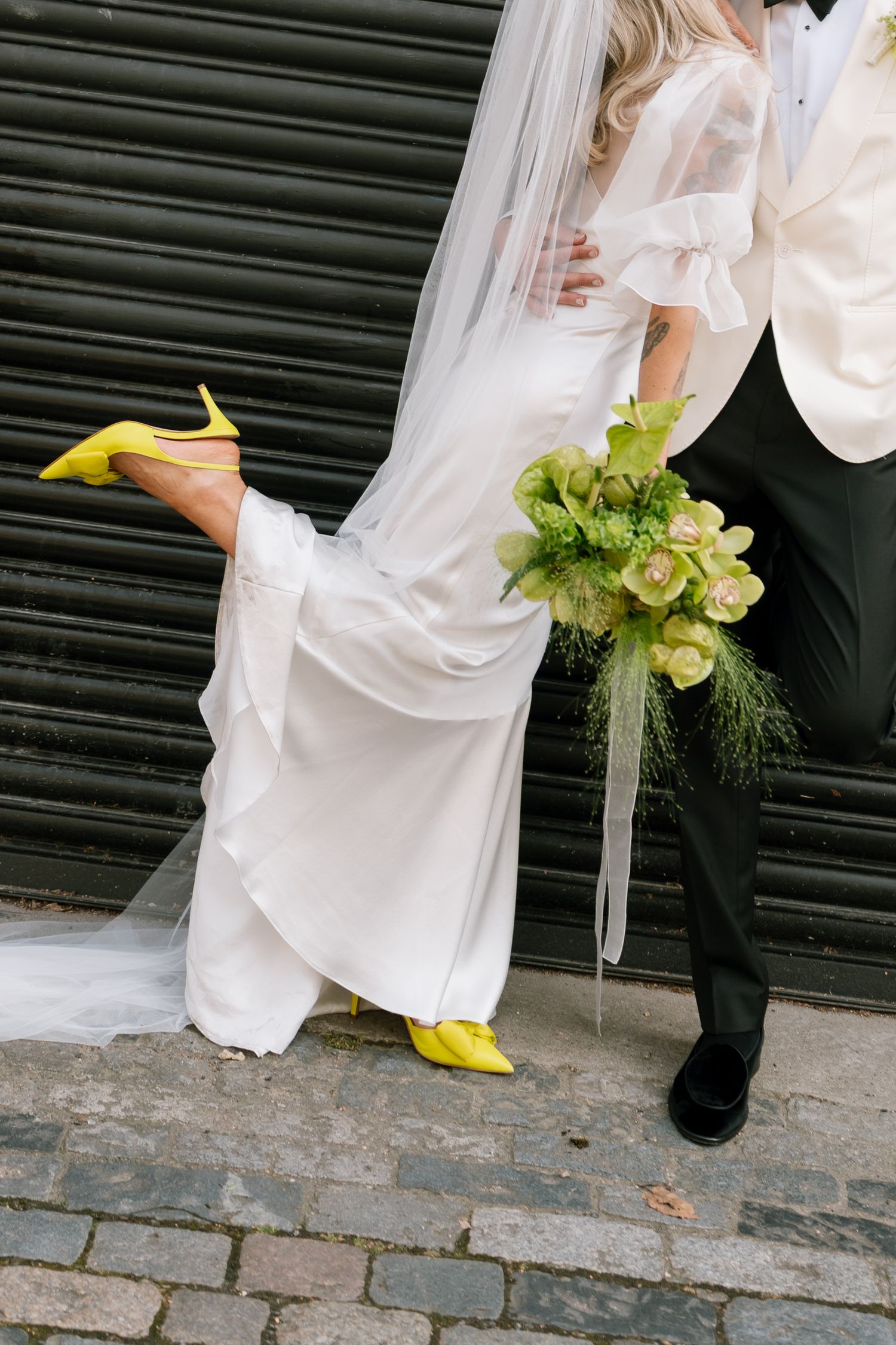 Close-up of wedding attire showing bright yellow shoes and green bouquet details.