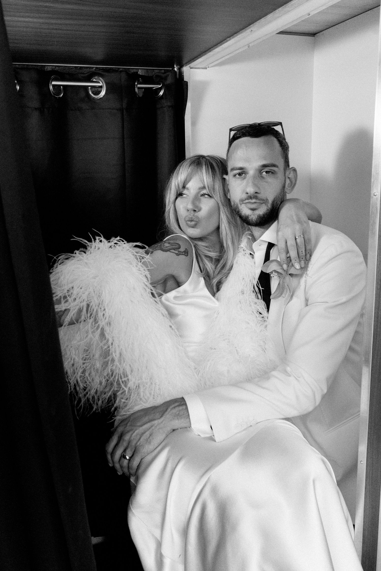 Playful photo series in white outfits with feather accessories in photo booth setting.