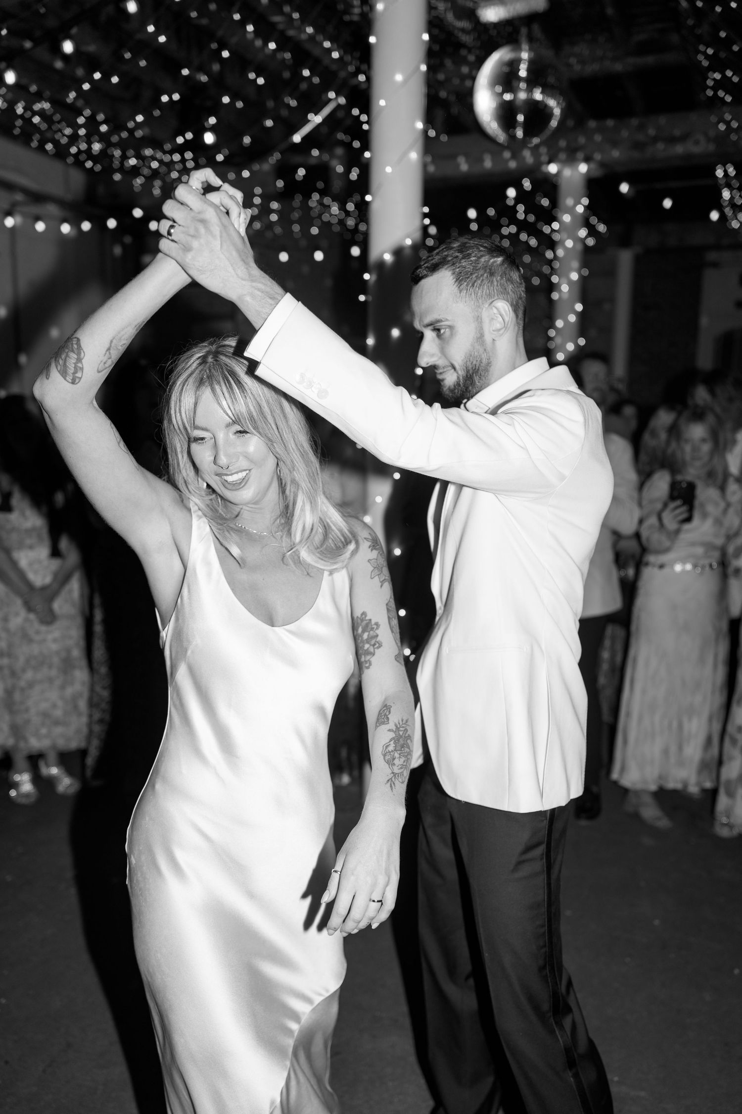 A couple dances together under twinkling lights at their wedding reception.