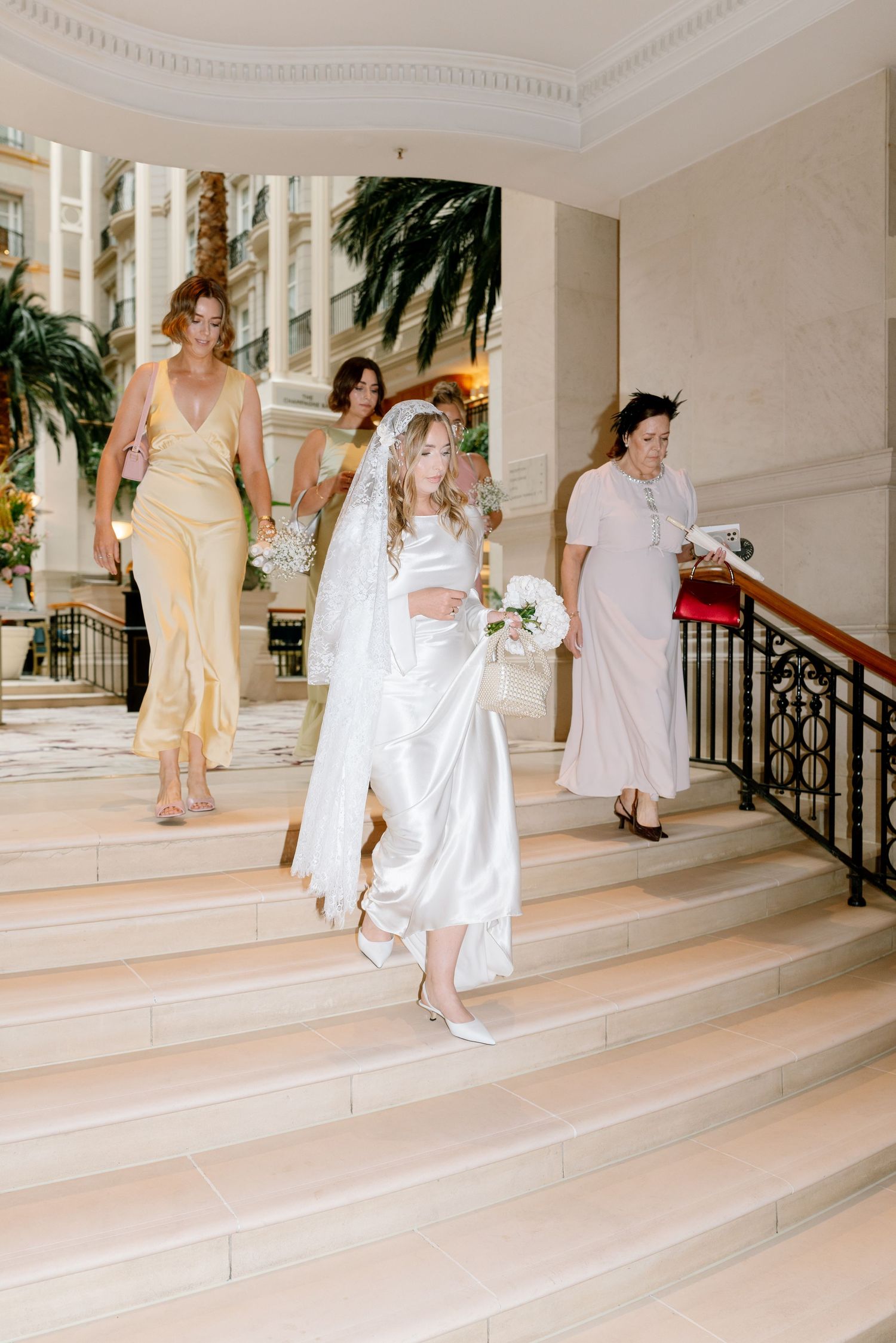Series showing people in light colored dresses descending elegant marble stairs with ornate railings.