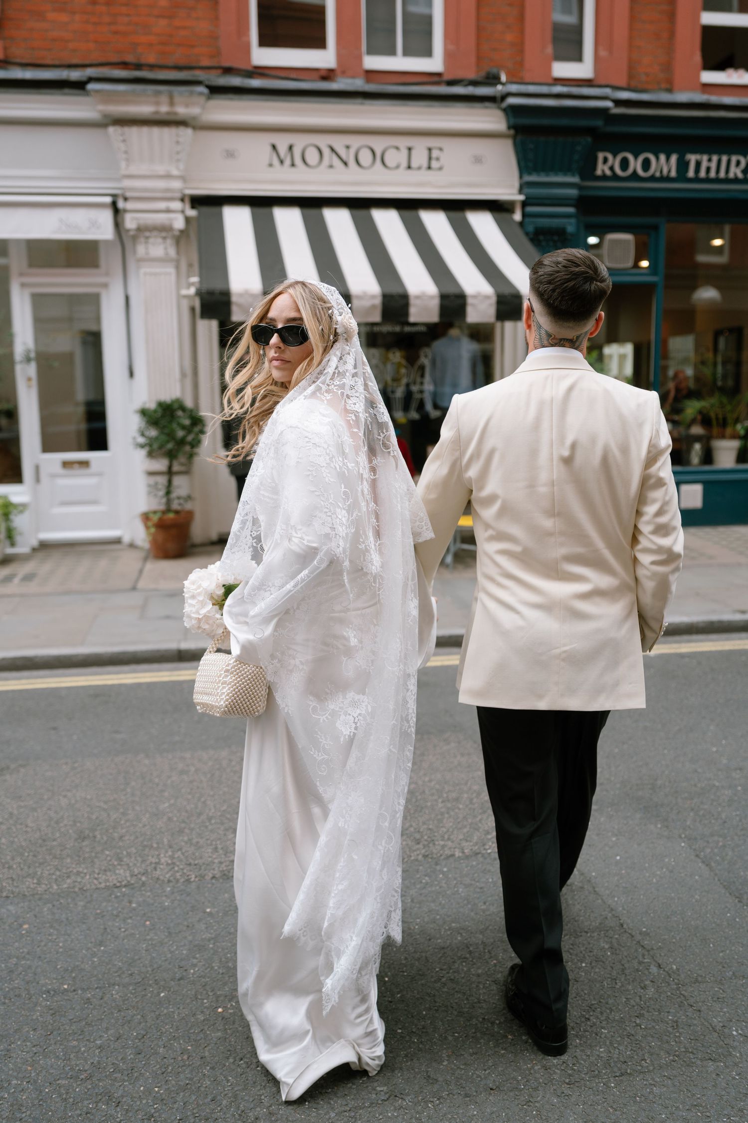 A couple walks past shops on a London street with the Monocle storefront visible.