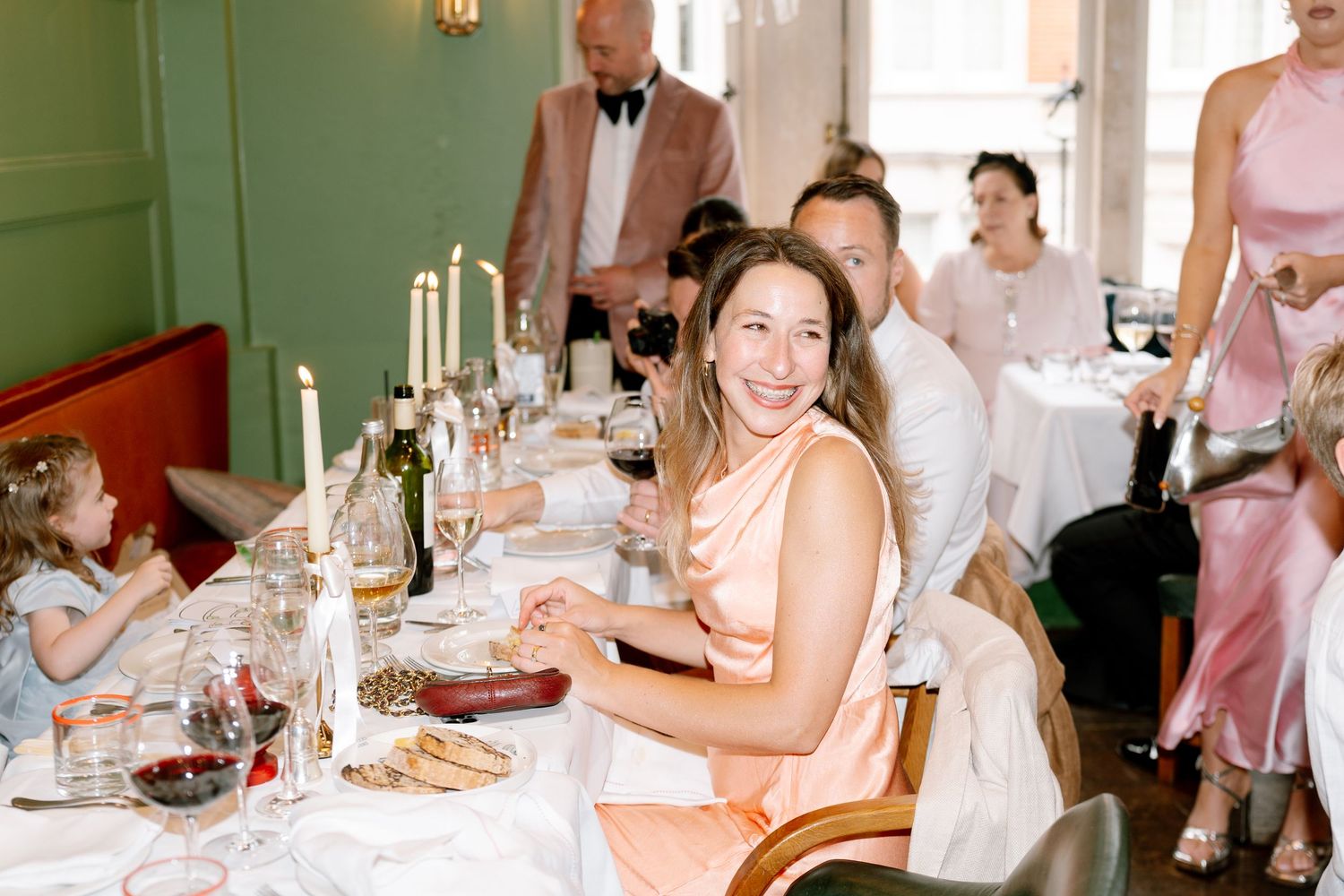 Wedding reception table setting with guests in pink and white attire celebrating.