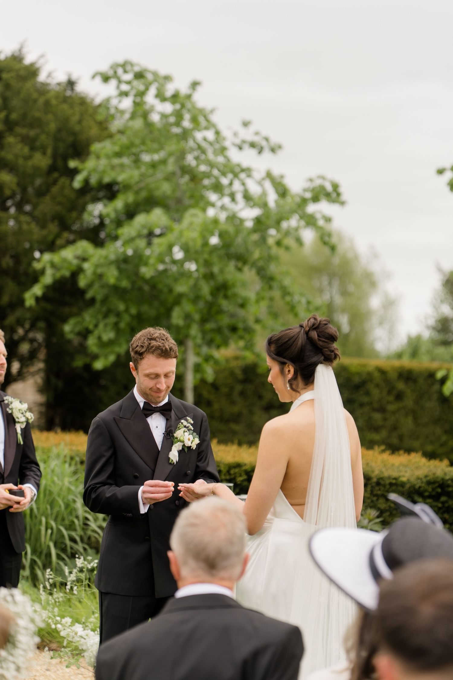 Groom placing wedding ring on brides finger during outdoor ceremony at a lush English garden venue.
