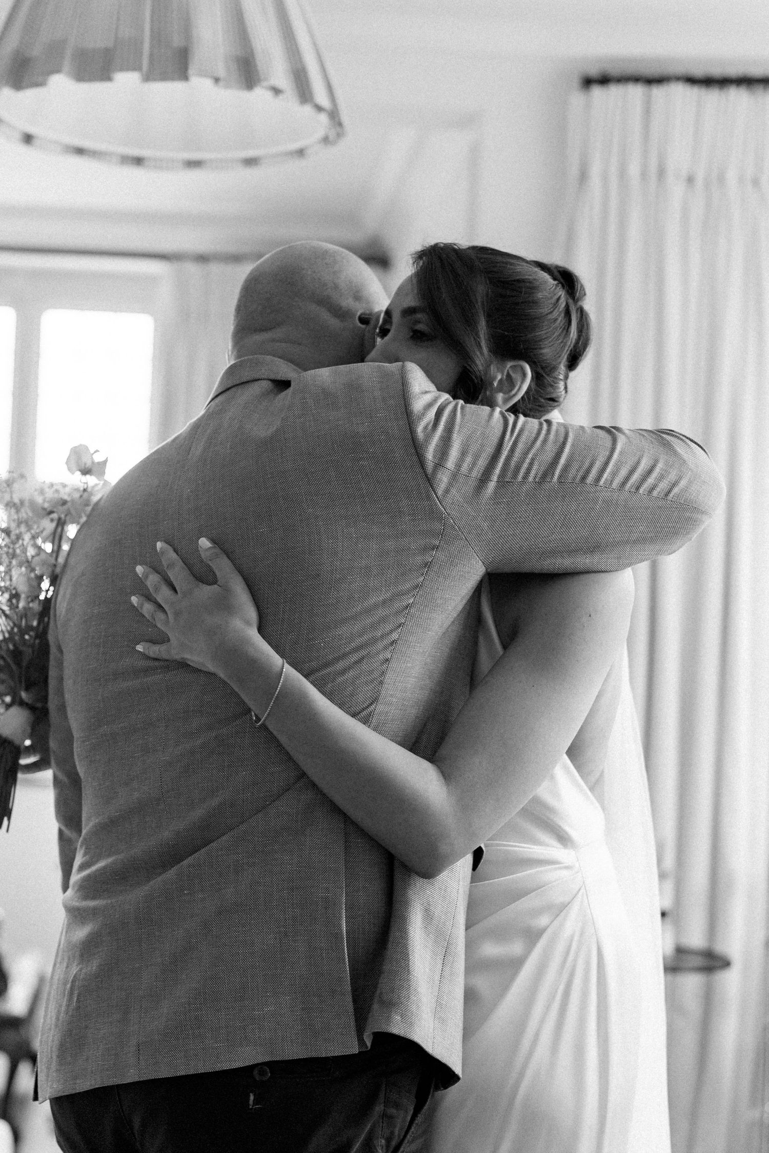 Bride and groom sharing an emotional embrace during wedding preparations in a bright interior room.