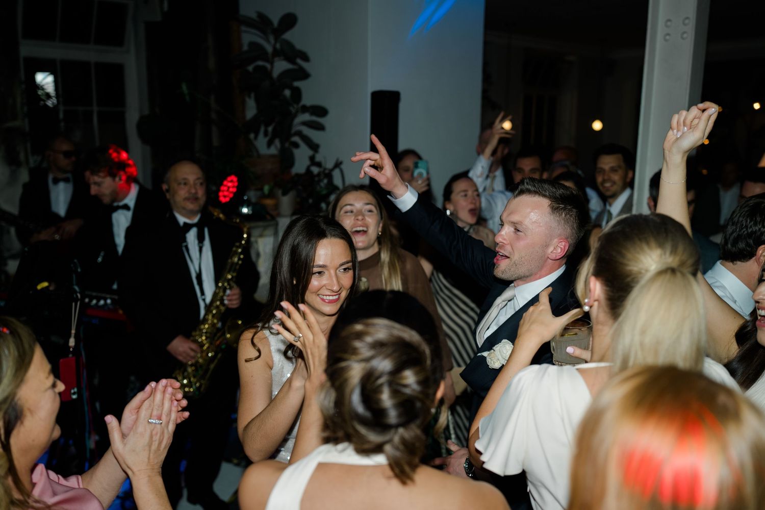 Lively wedding dance floor with guests celebrating, raising hands, and dancing with the couple.