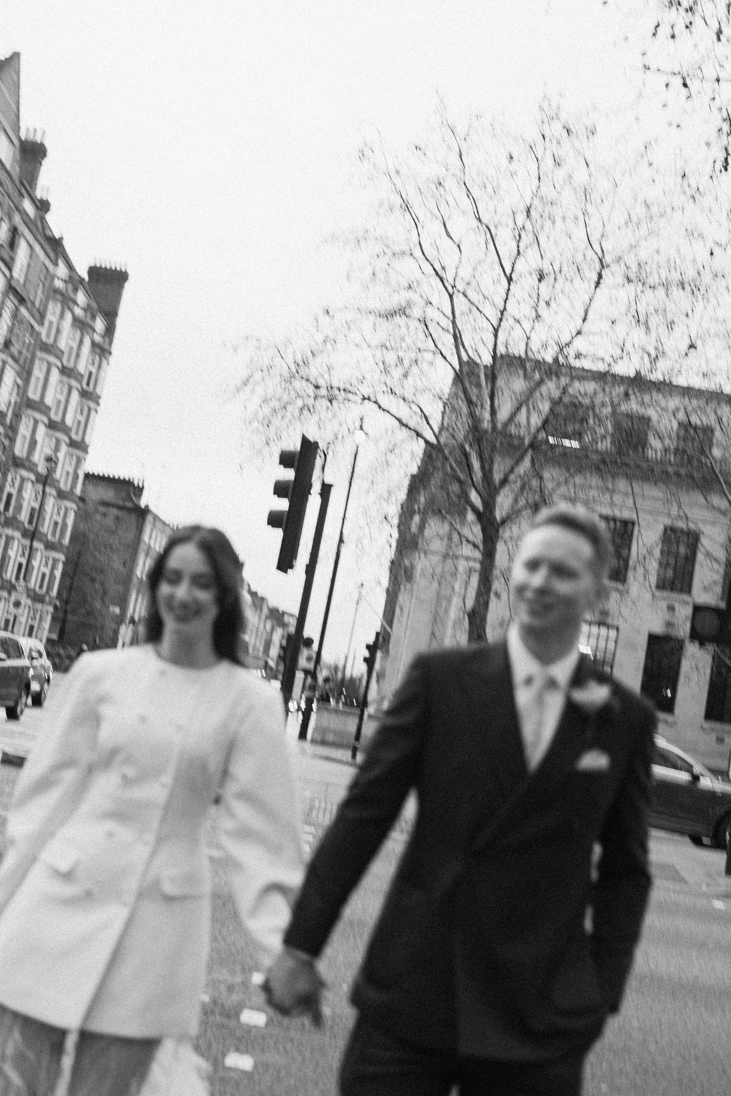 Black and white photo of bride and groom holding hands crossing a London street on their wedding day.