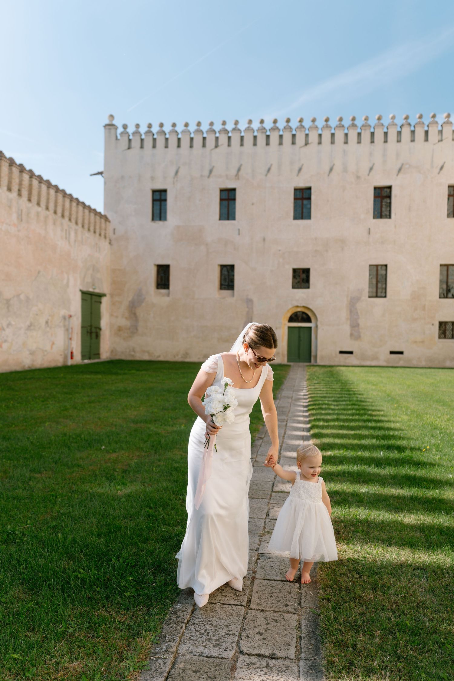 Elegant wedding scene at historic castle with stone path and manicured lawn.