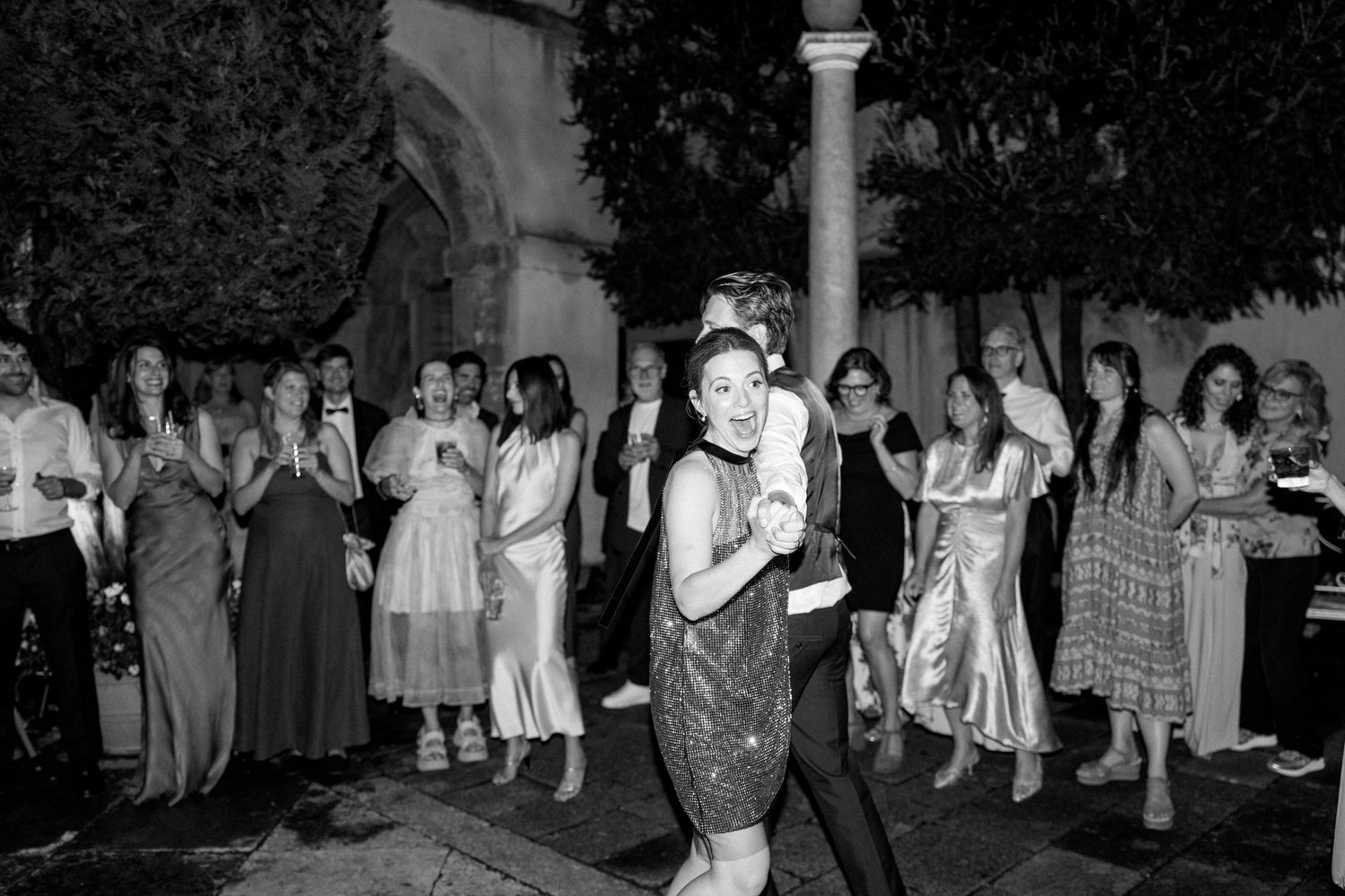 Large group of party attendees dancing outdoors under evening sky.
