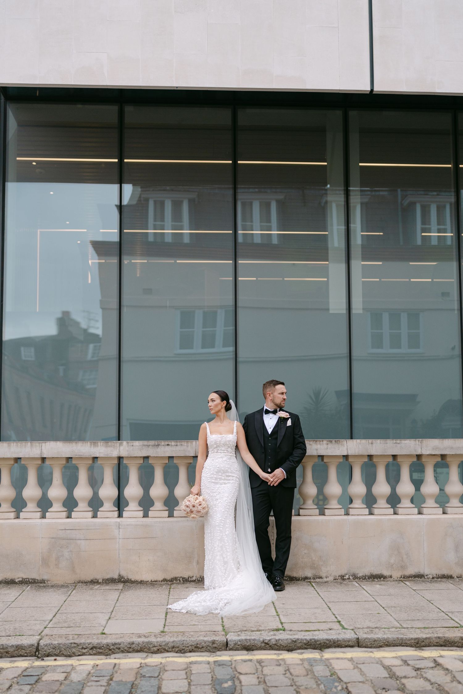 Elegant wedding portraits against modern glass architecture with stone balustrade details.