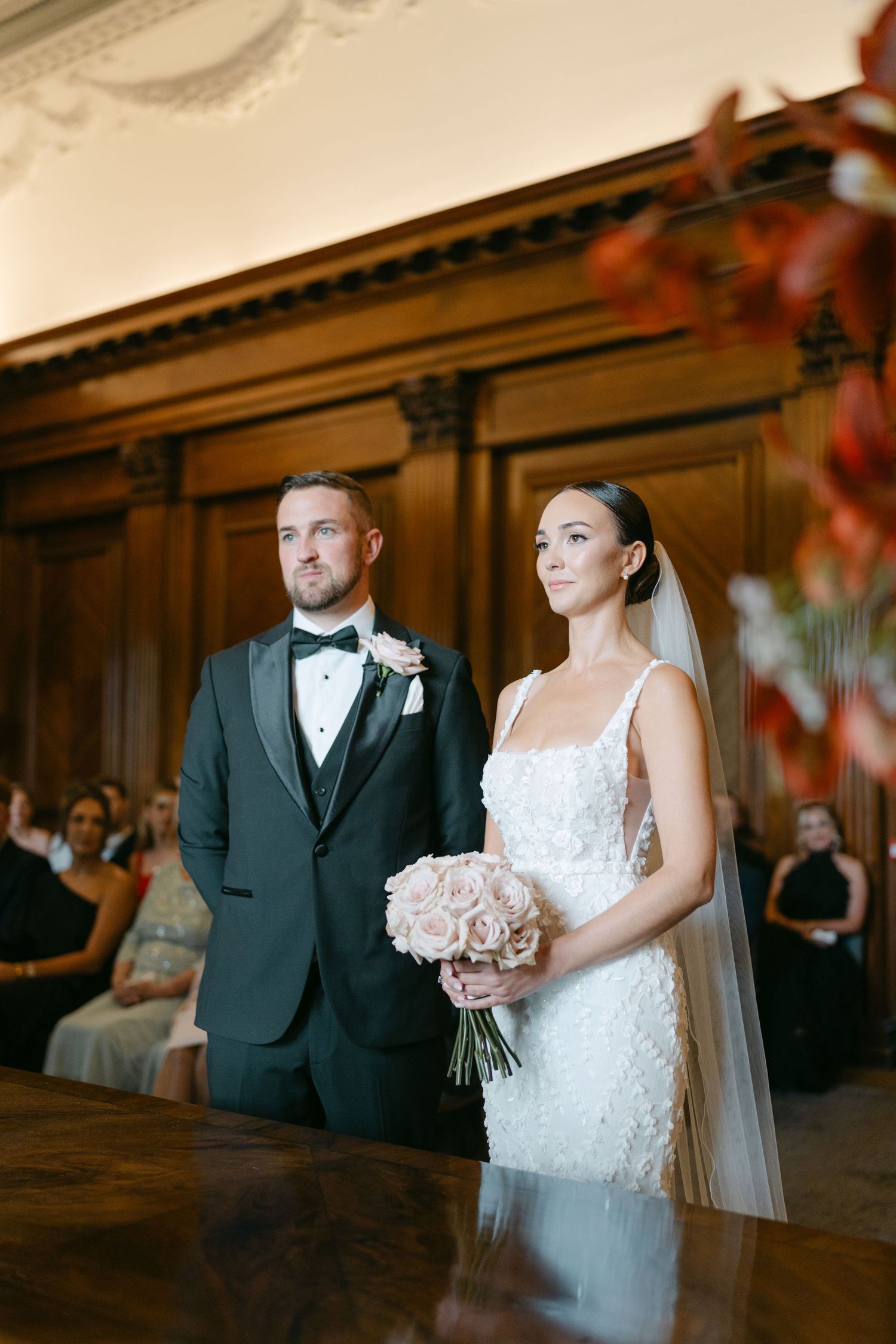 Wedding couple stands in an elegant wood-paneled venue with autumn-colored decorations.