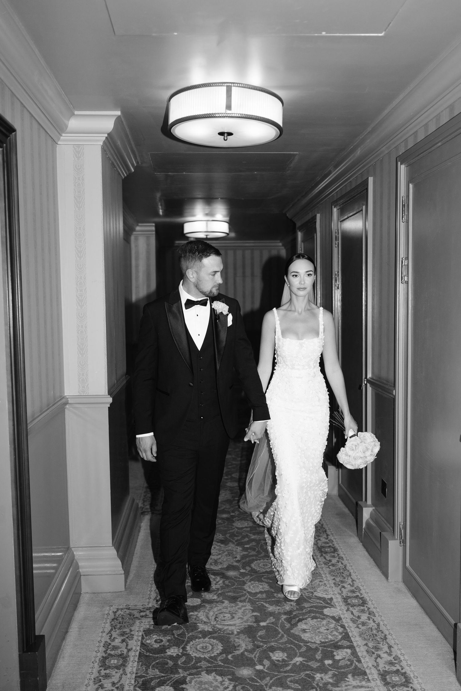 Wedding couple strolls through luxurious hallway with decorative lighting.