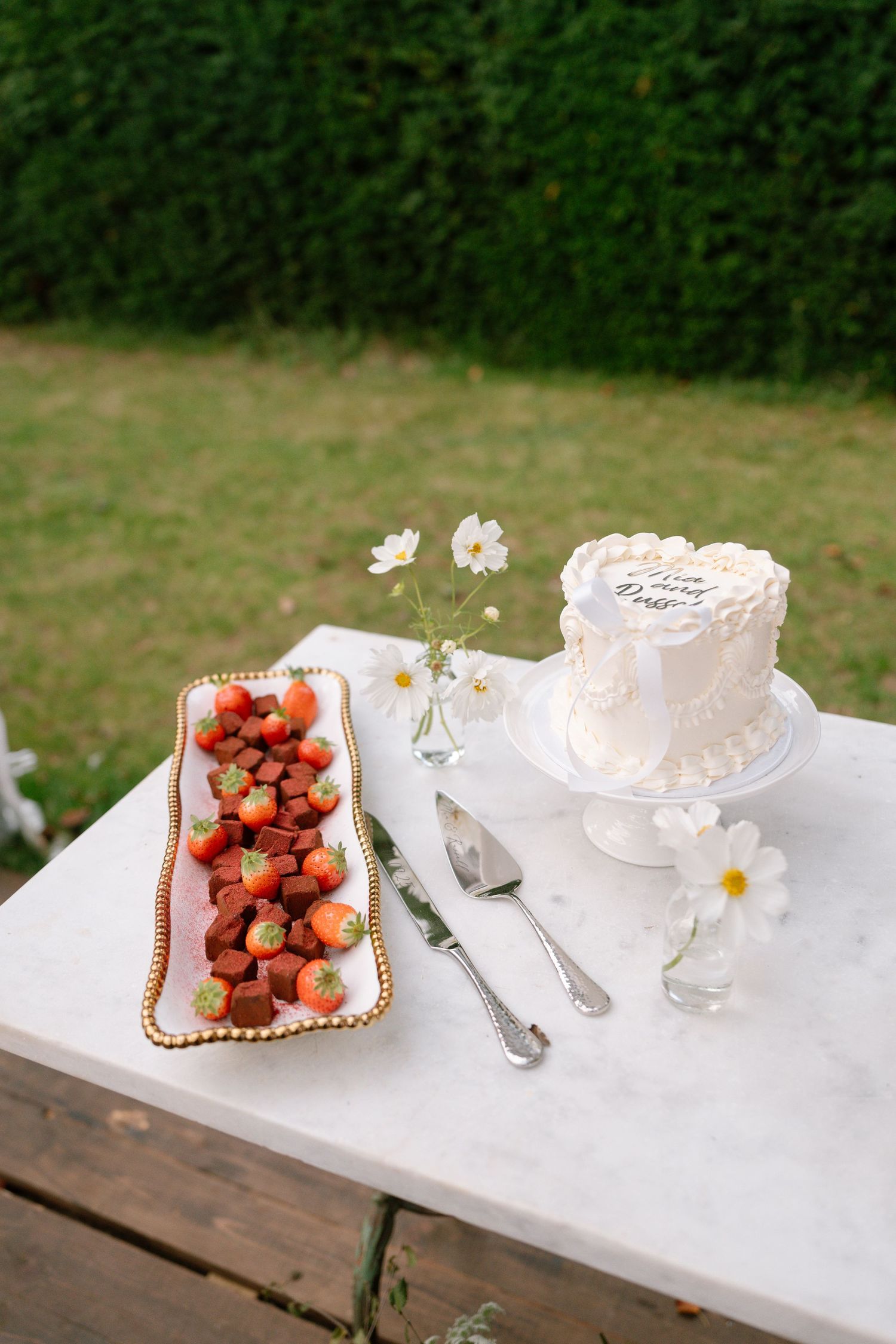 Dessert table with fresh strawberries, white flowers, and serving plates on white tablecloth.