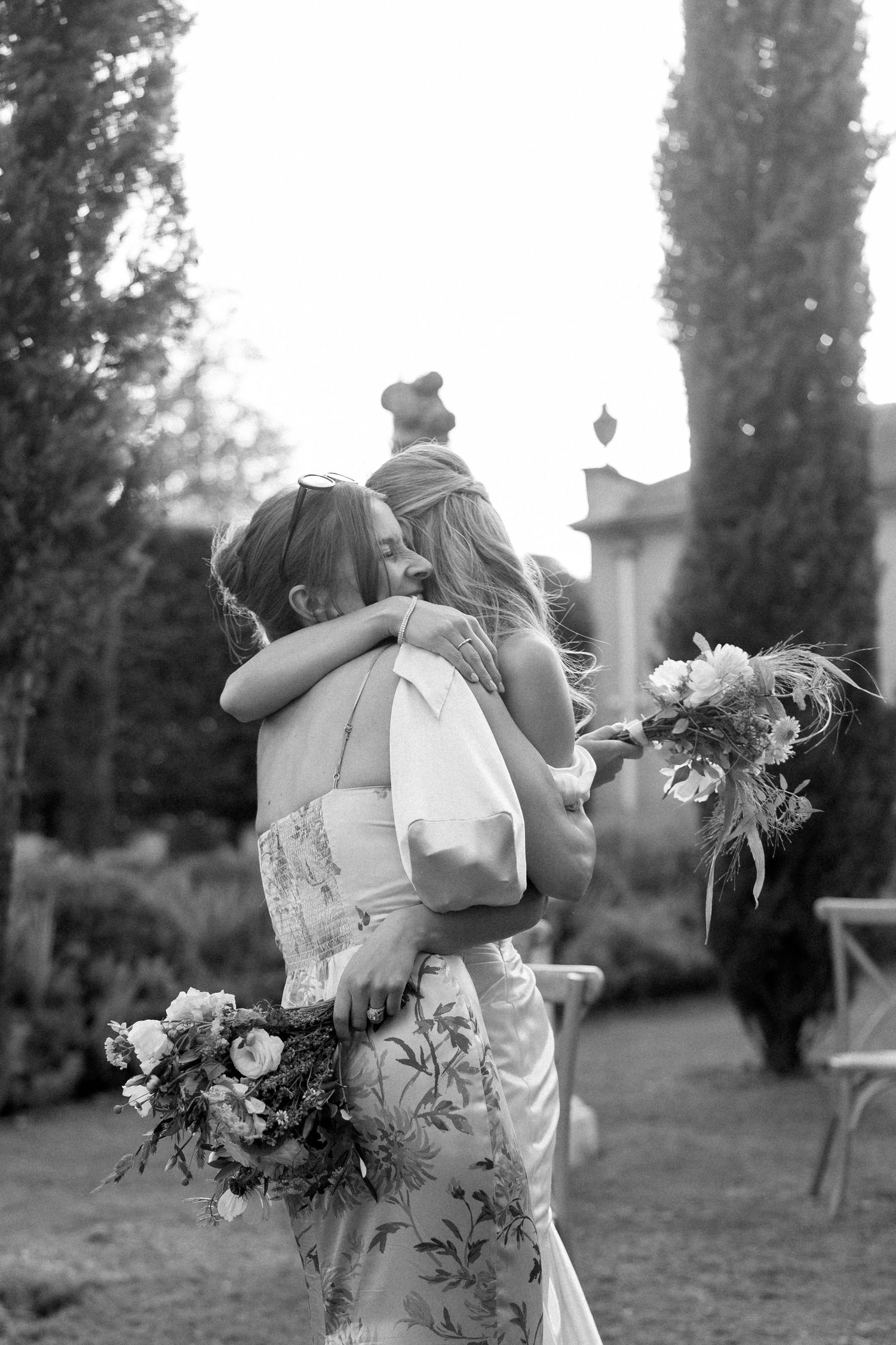 A tender embrace between two people holding floral bouquets in a garden setting, captured in black and white.
