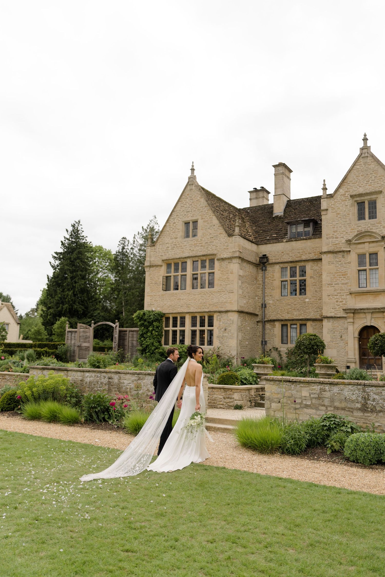 Bride and groom embracing in garden of stunning Cotswolds stone manor wedding venue.