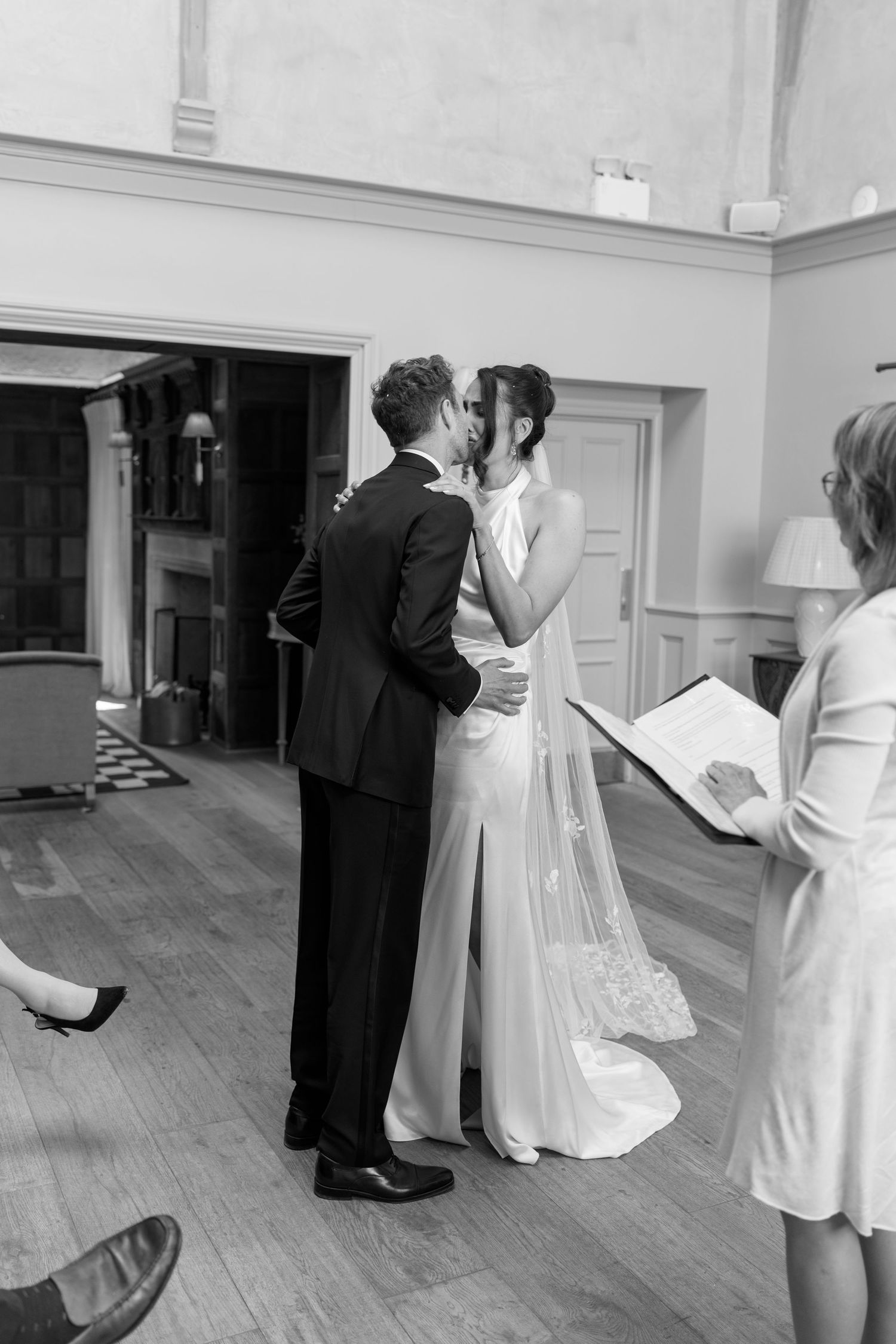 Bride and groom share their first kiss during an intimate indoor wedding ceremony in black and white.