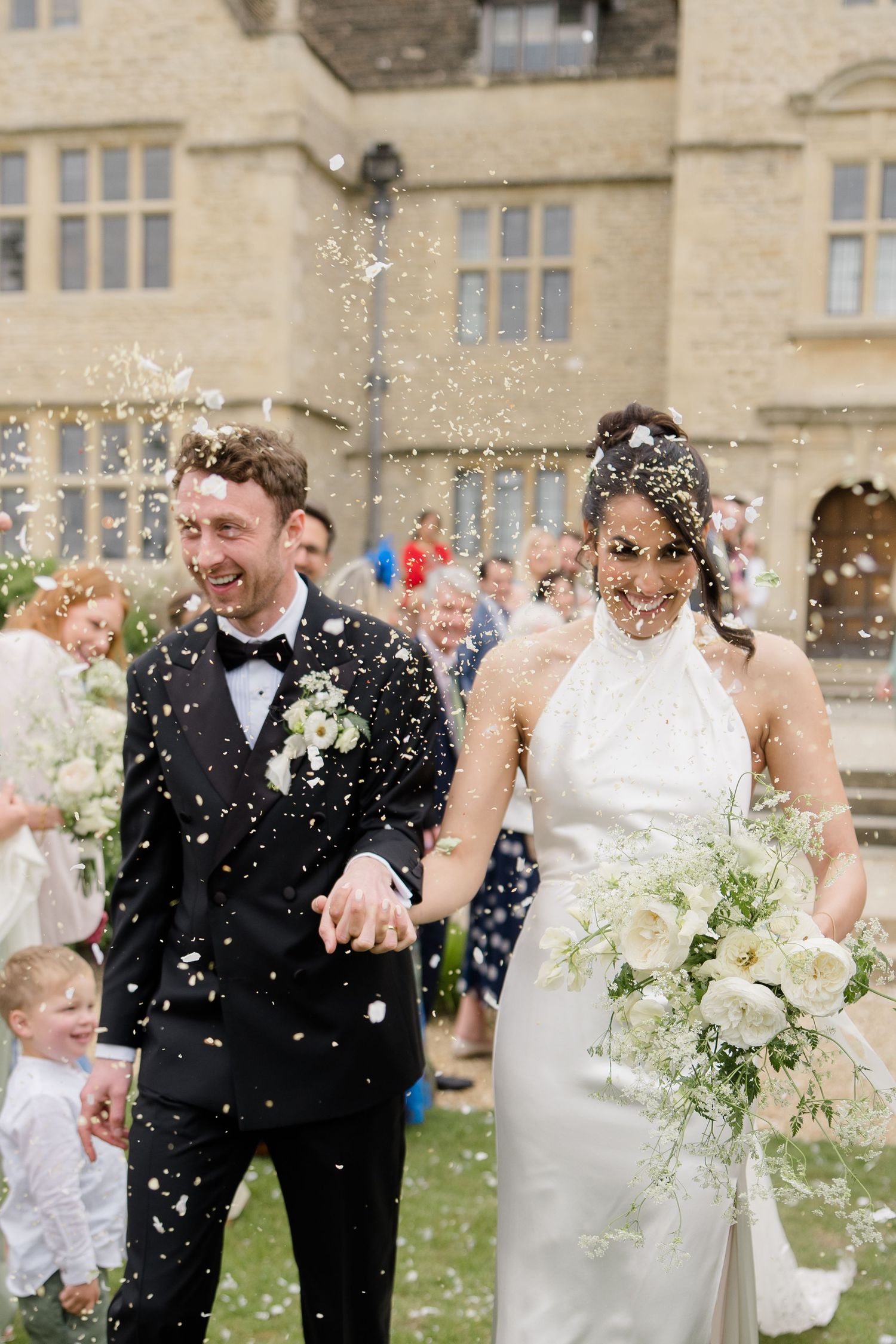 Joyful newlyweds walk through confetti shower outside historic stone wedding venue.