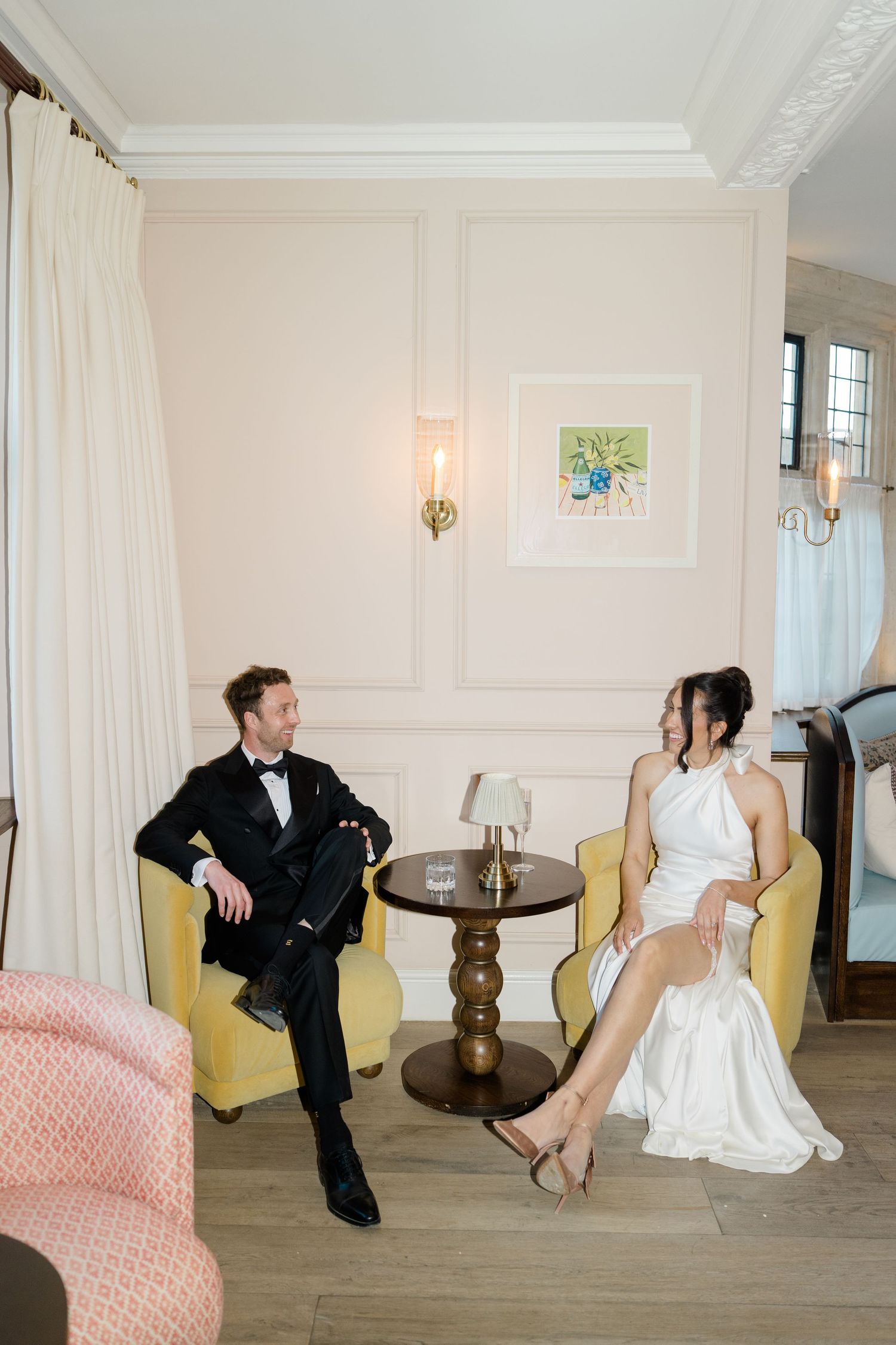 Bride and groom relax in yellow armchairs in an elegant pastel-toned room during their wedding.