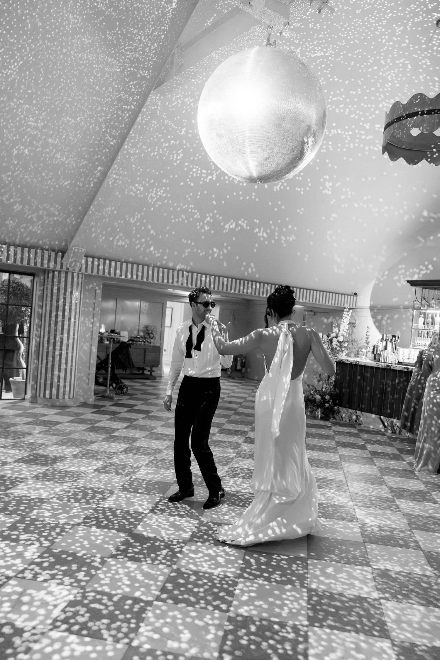 Black and white photo of bride and groom sharing first dance under a glittering disco ball.
