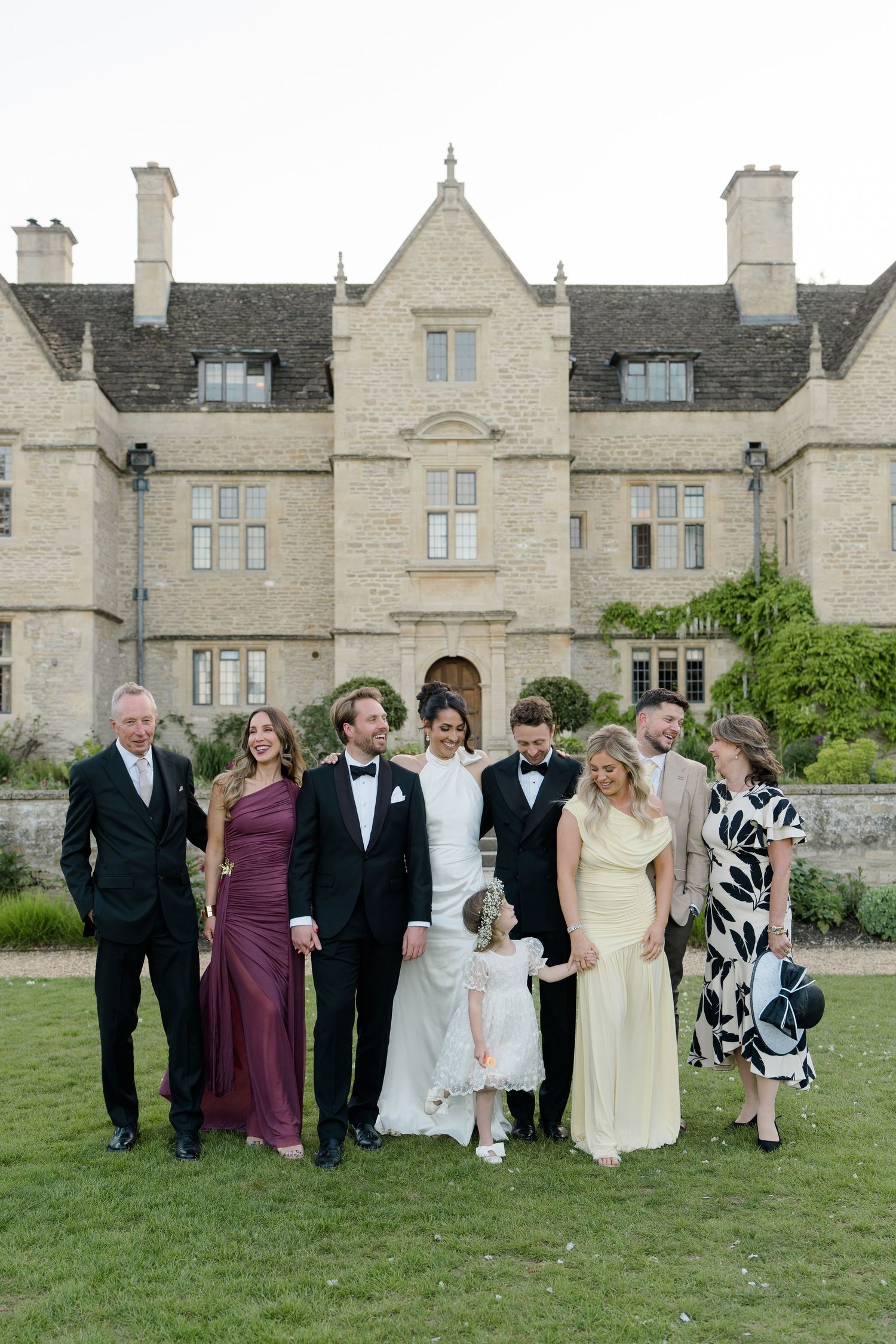Wedding party group portrait with bride, groom, family, and guests on lawn before stone manor.