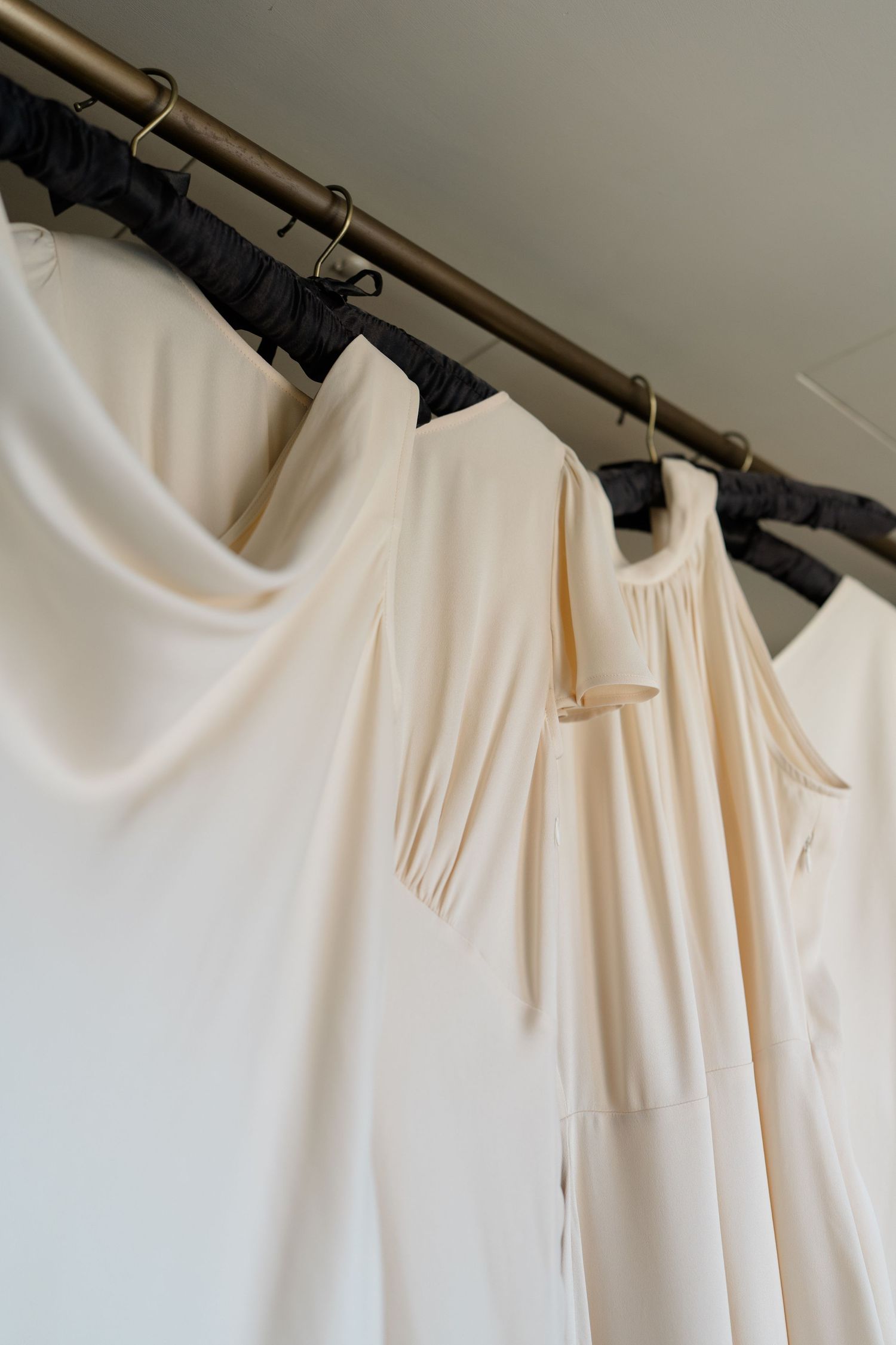 Ivory bridesmaid dresses hanging on a brass clothing rack with black hangers.