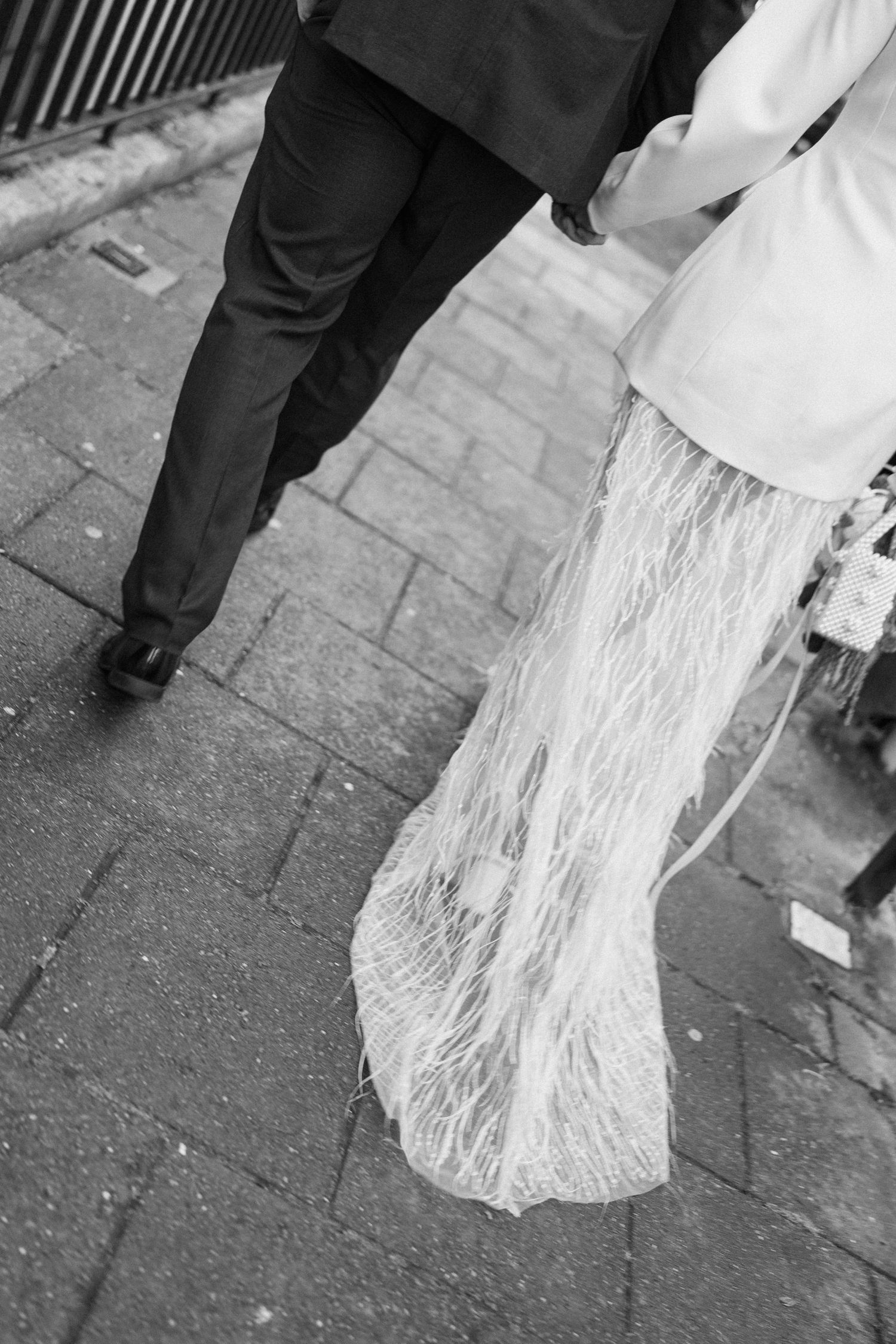 Black and white photo of bride and groom walking on cobblestone street.